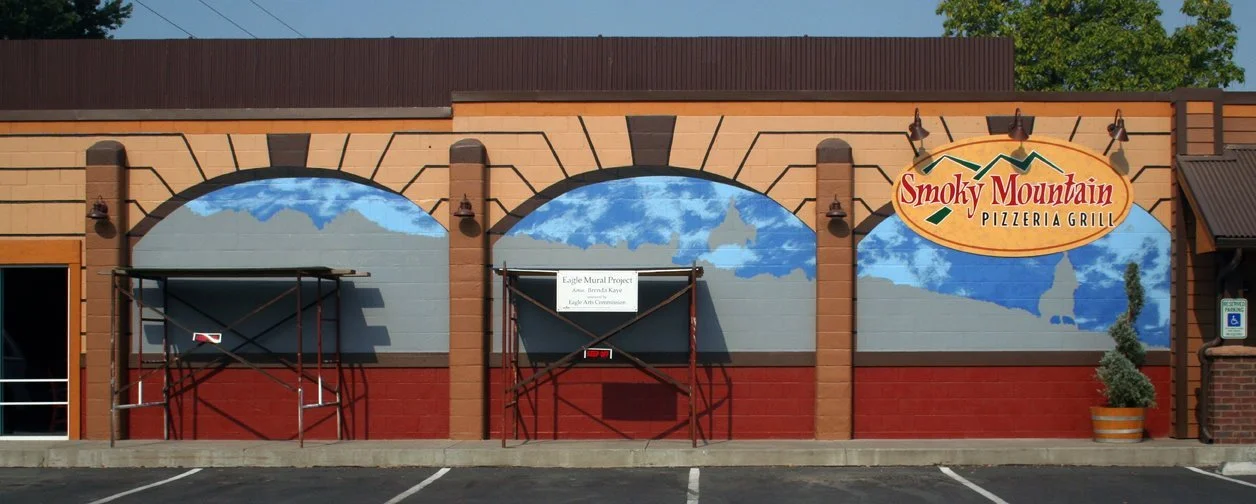 Exterior of Smoky Mountain Pizzeria Grill with murals of mountains and clouds, scaffolding in front, and a pot with a plant.