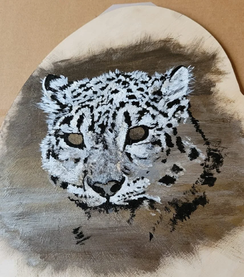Painting of a snow leopard's face on a circular canvas with a brown background.