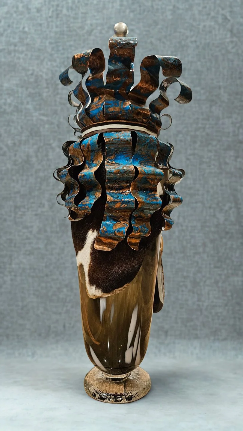 Decorative glass vase with intricate, curly blue and brown patterns, adorned with a small silver topper, standing on a wooden surface against a gray background.