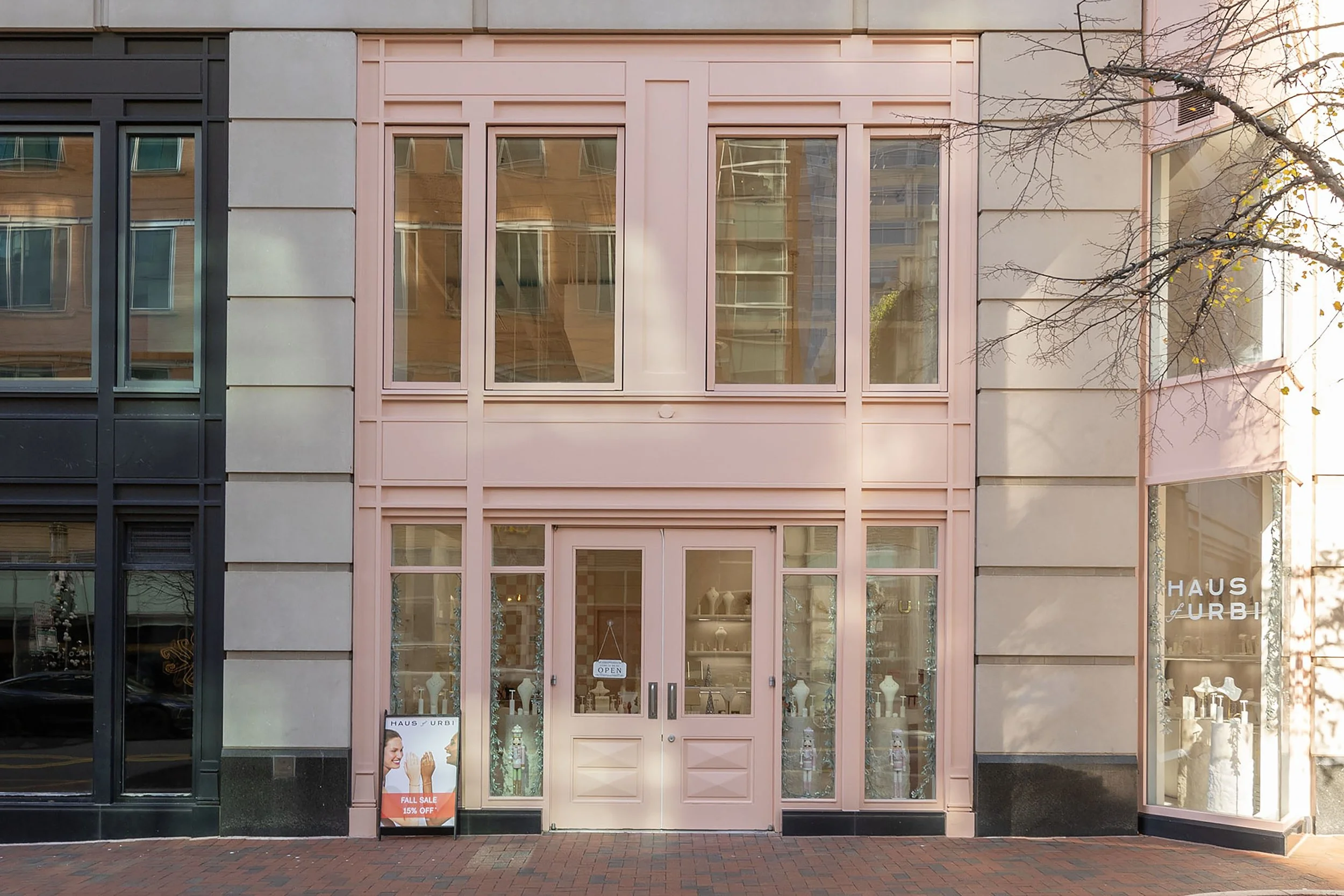 The storefront of a jewelry store with large windows, pink trim, and a sign for a fall sale.