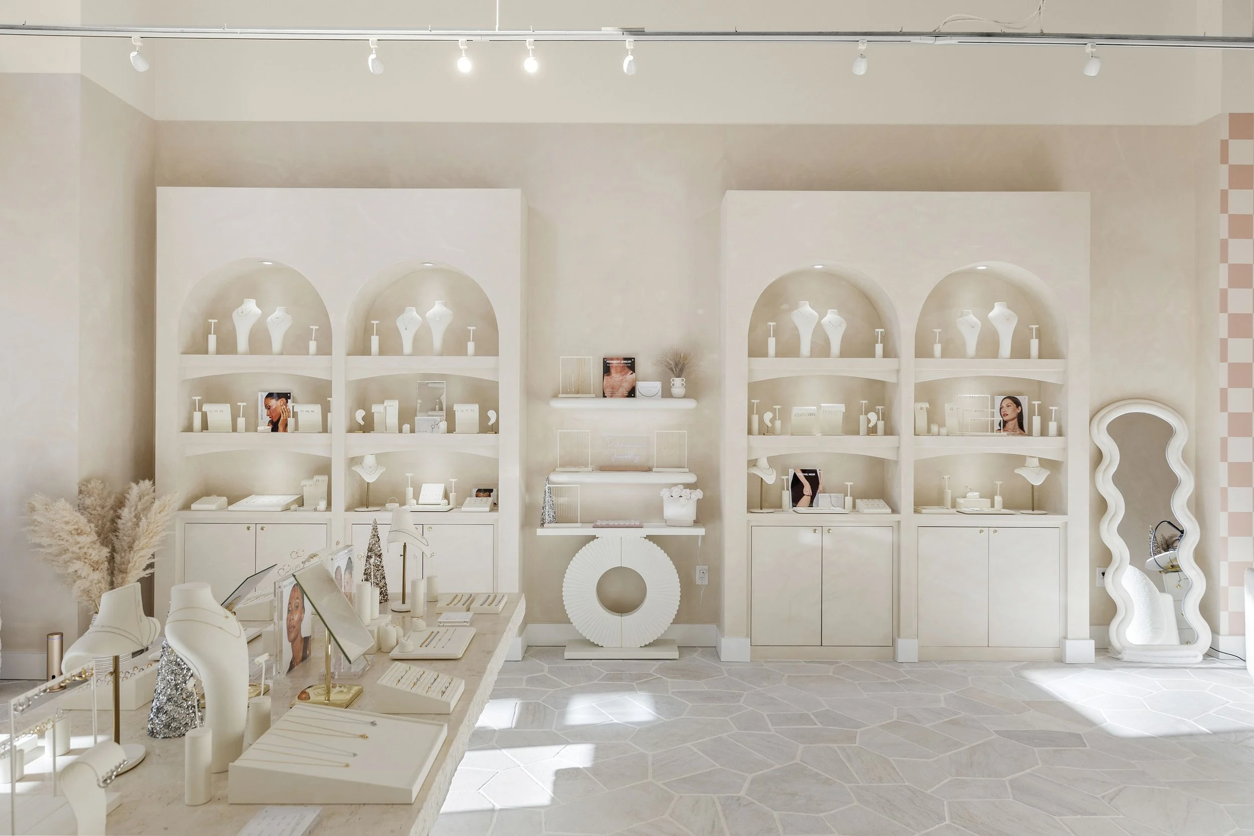 Interior of a jewelry or cosmetics store with white display shelves, mannequins, vases, and framed photos, all in a minimalist design.