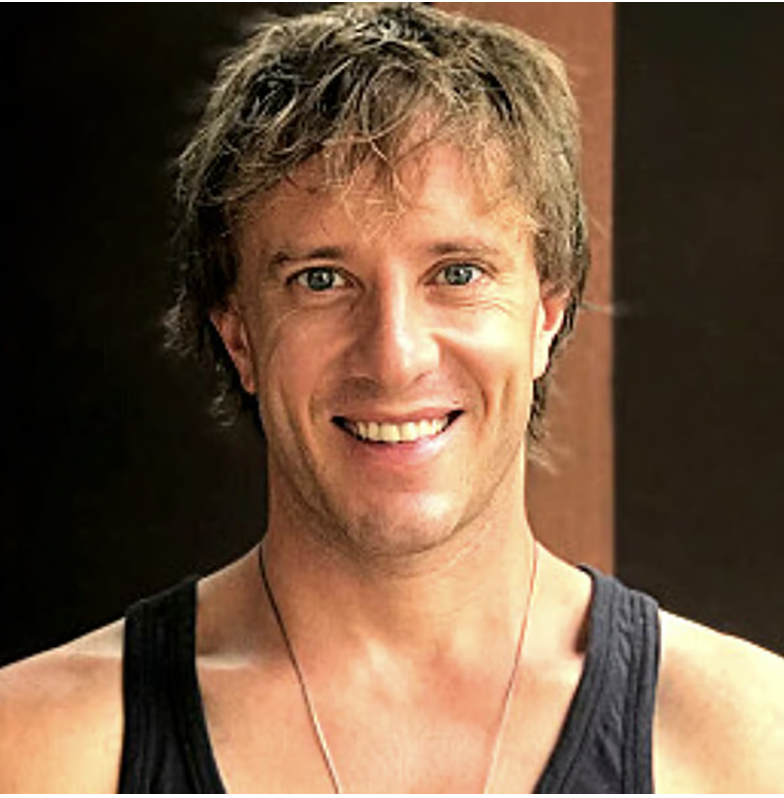 Smiling person with short hair wearing a black tank top indoors.
