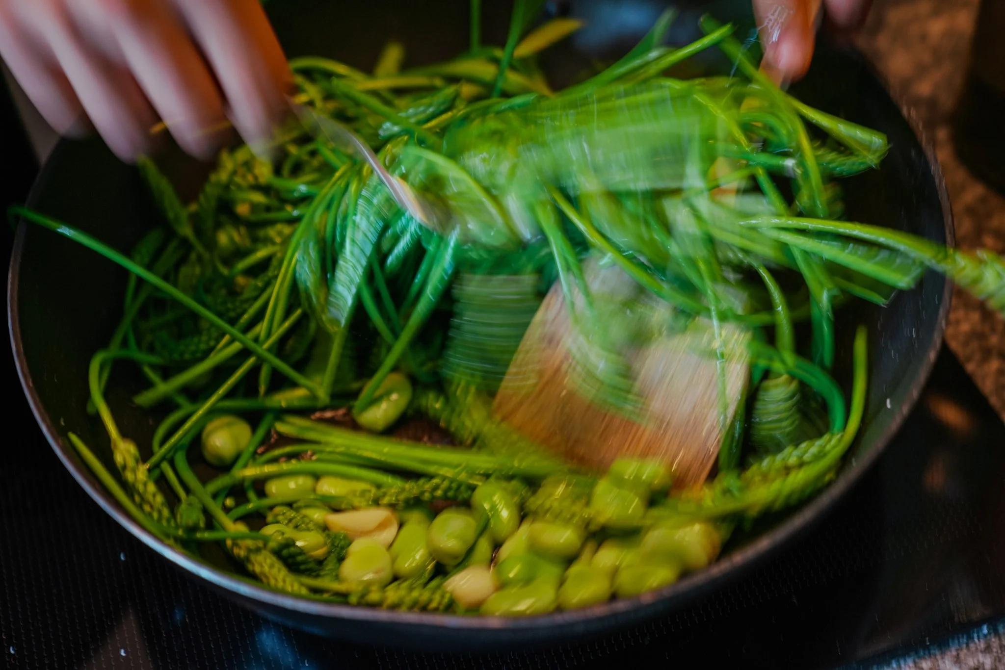 Cooking green vegetables in a pan with a wooden spatula and fork.