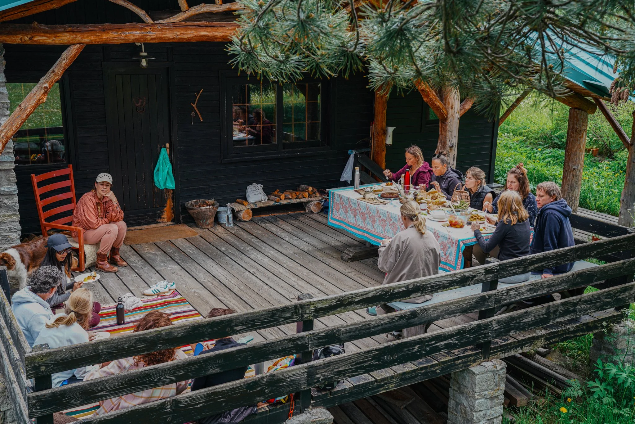 Group gathering on a cabin porch with a meal on a table and a picnic scene on the floor.