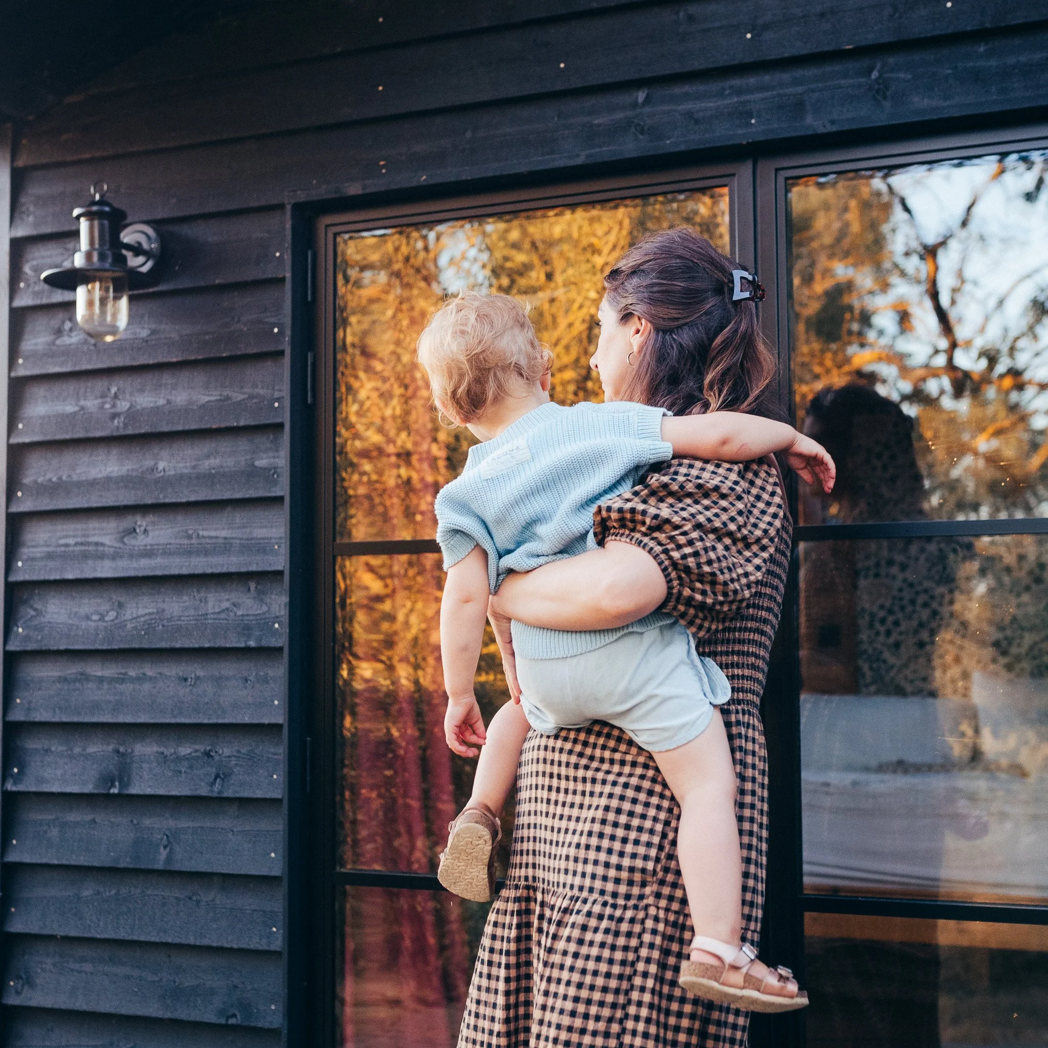 Mother holding her child outside their lodge during a relaxed family moment.