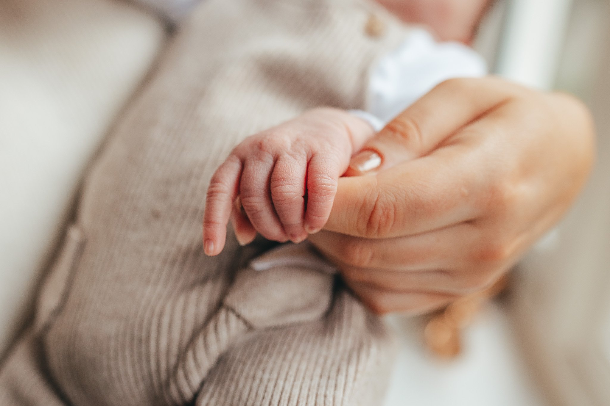 Mother holding her newborn baby's hand during a relaxed at home newborn photography session in Suffolk