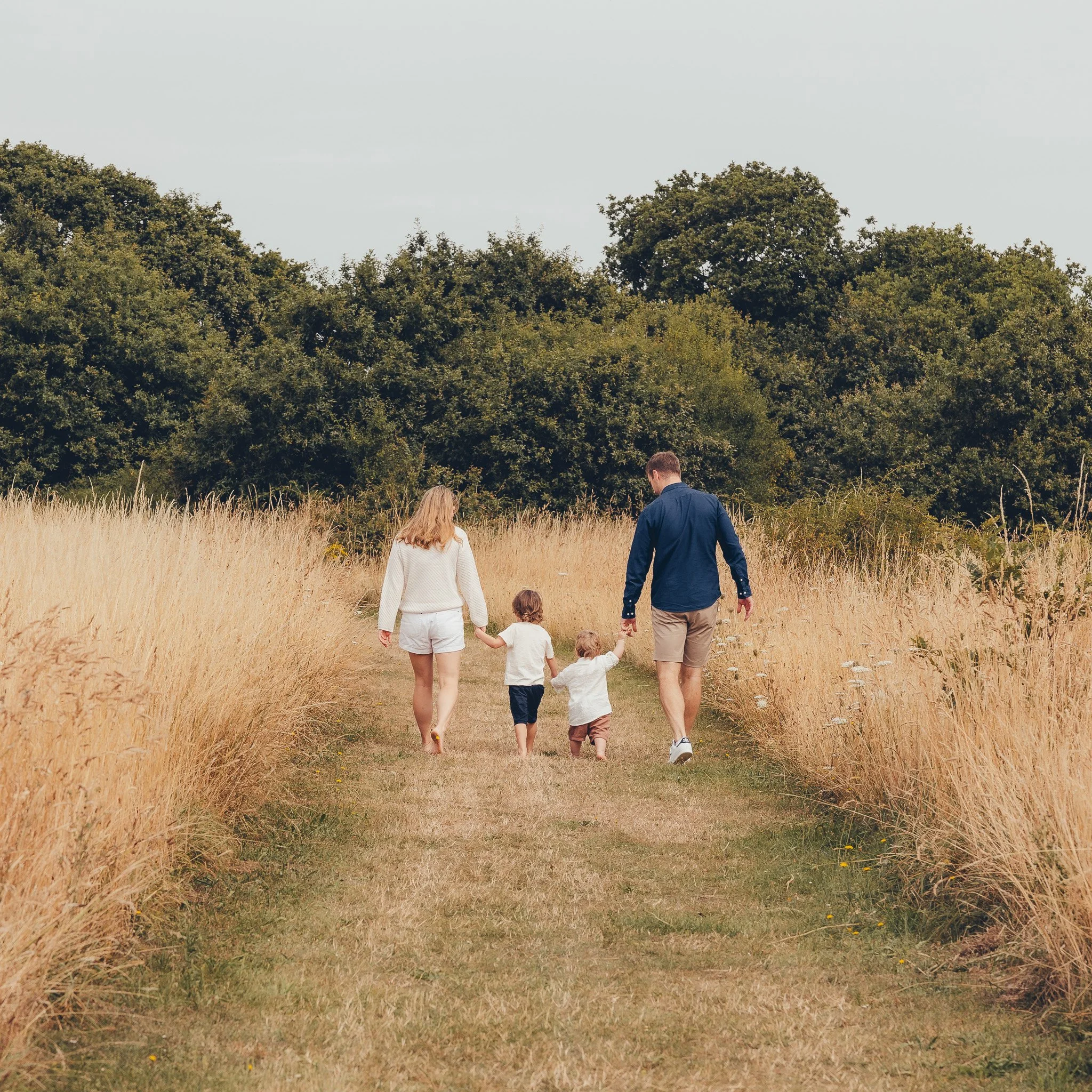 Family holding hands while walking through a meadow in Essex.