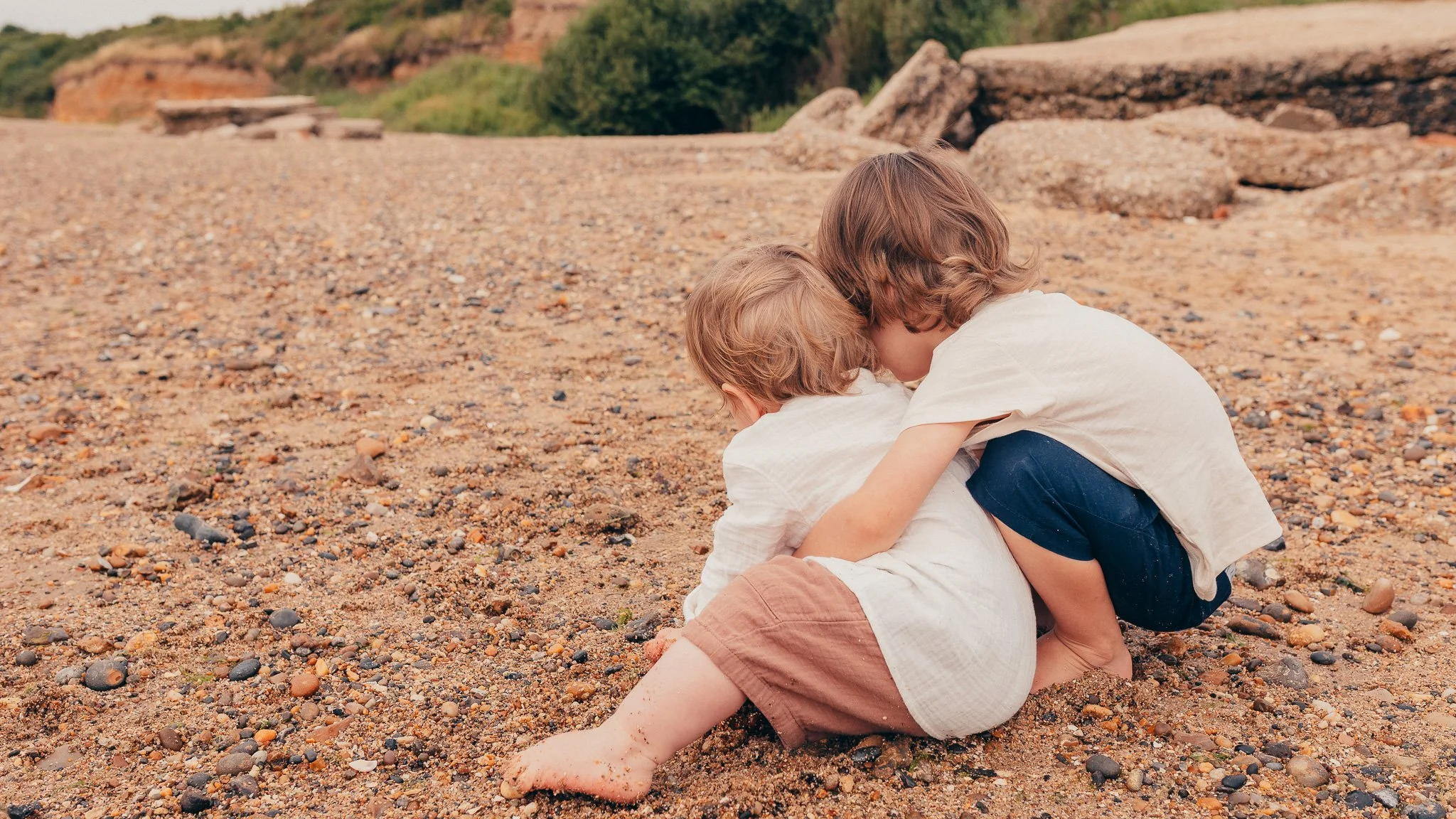 Siblings cuddling together on an Essex beach during a morning family photography session.