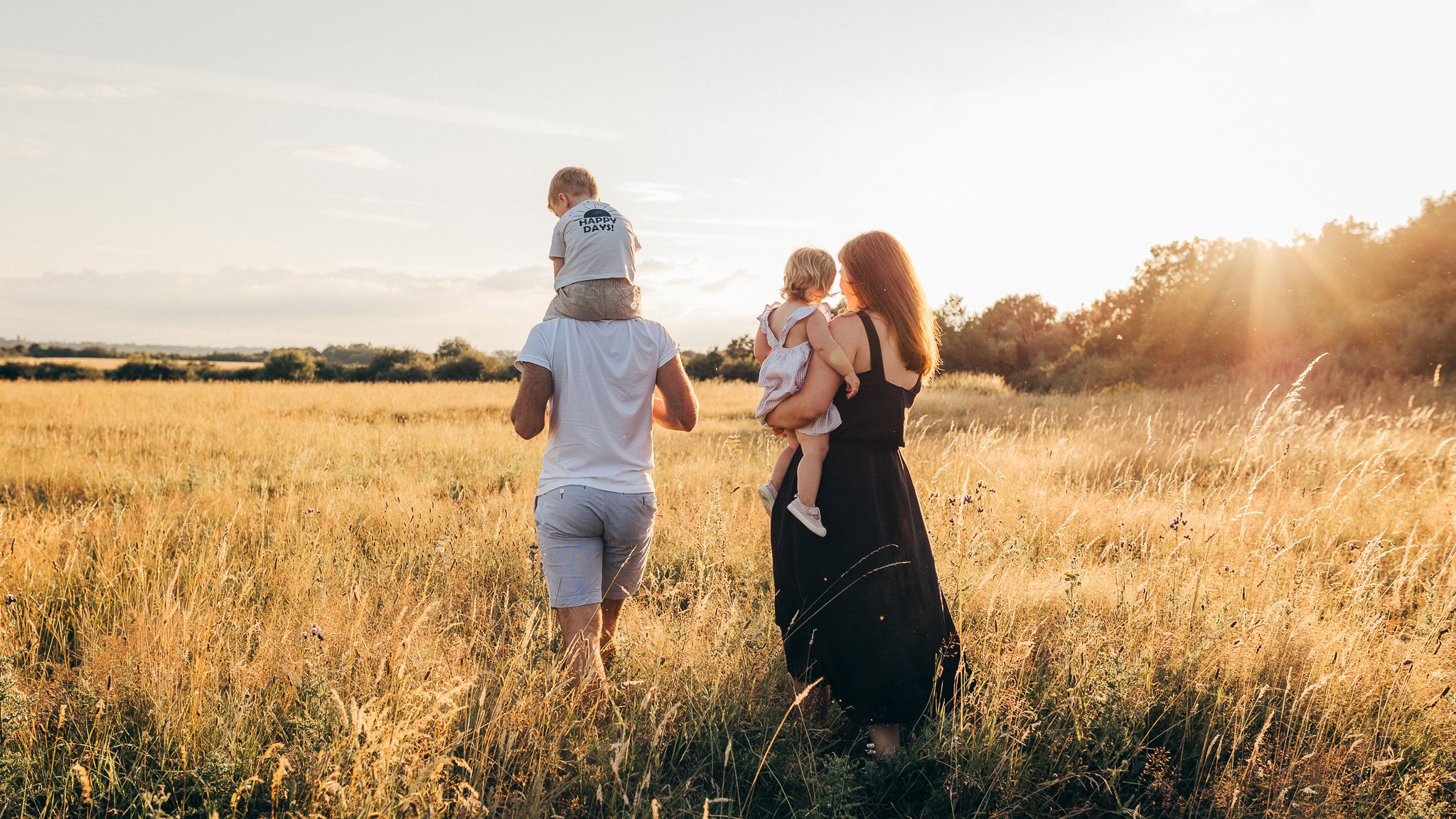 Young family walking through long grass at golden hour in the Essex countryside.