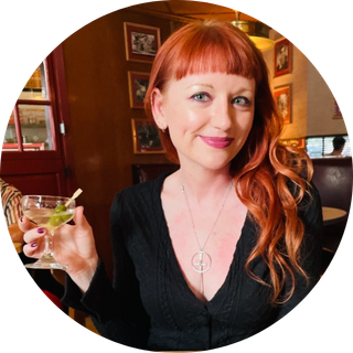 Woman with red hair smiling and holding a cocktail glass in a restaurant.