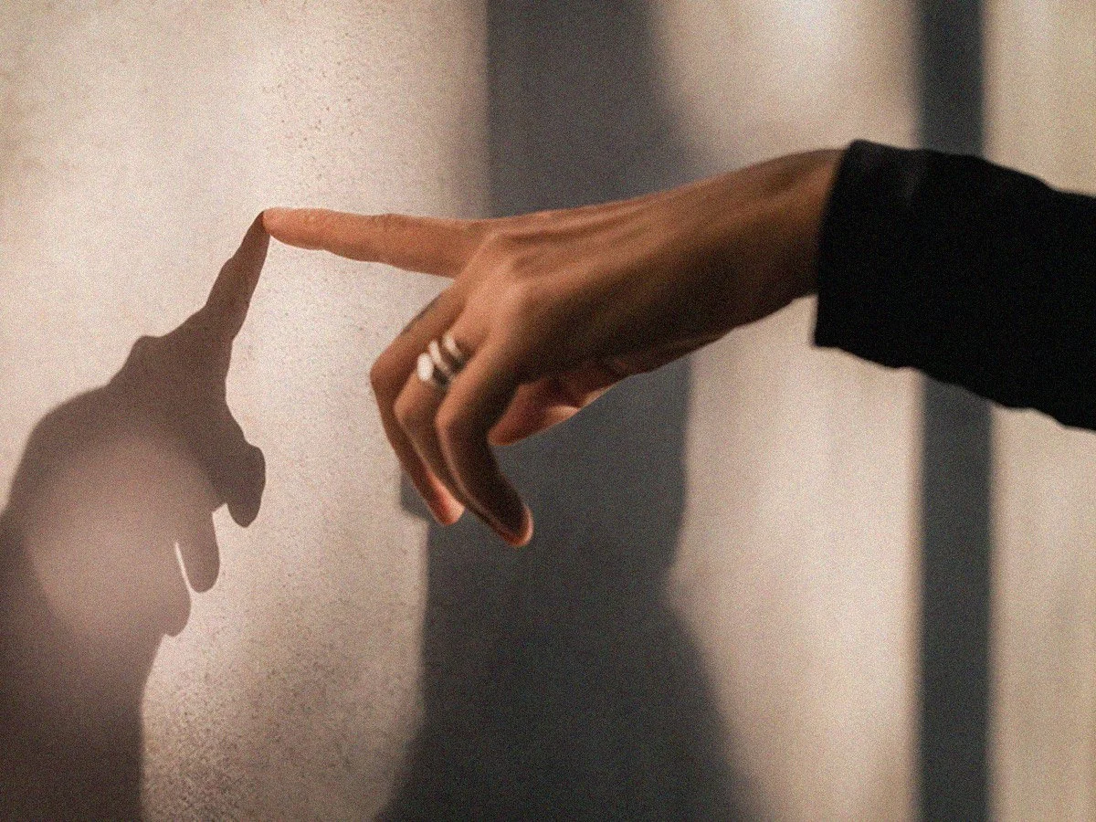 Close-up of two hands reaching out towards each other, with one hand touching a wall and casting a shadow that appears as the other hand.