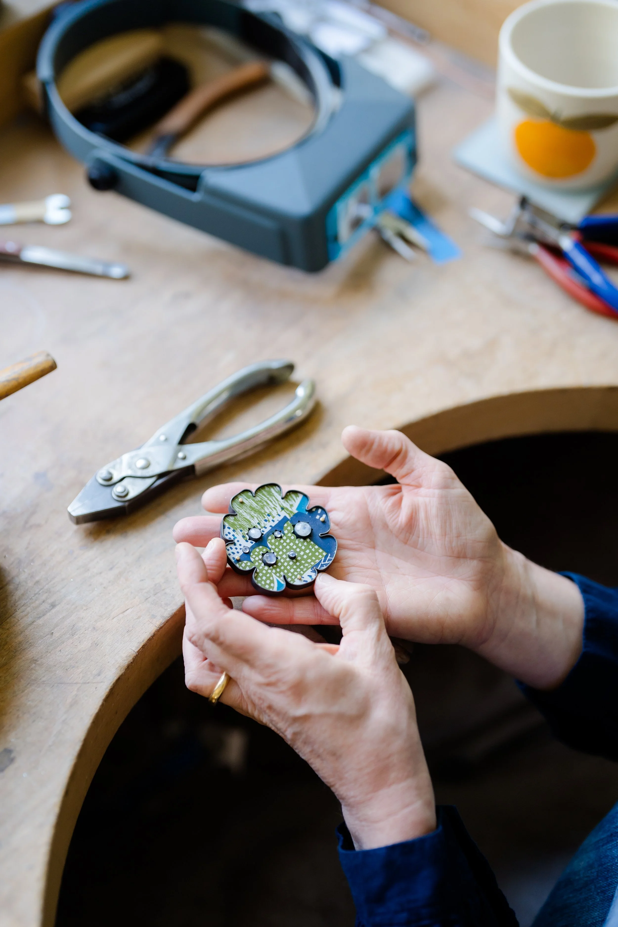 Lindsey Mann's hands holding a brooch above her studio workbench.
