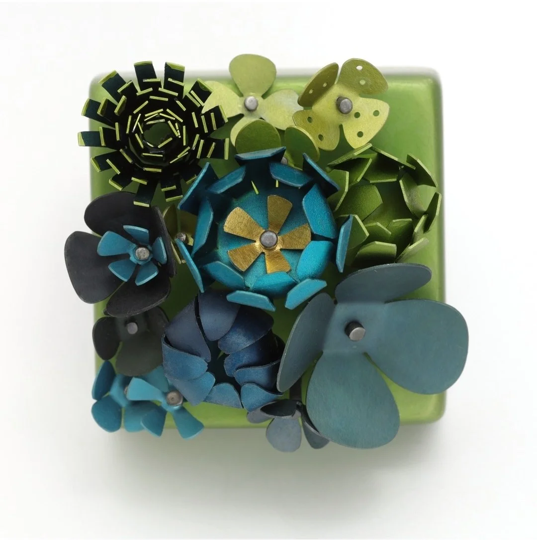 Colorful metal flowers arranged on a green block brooch.