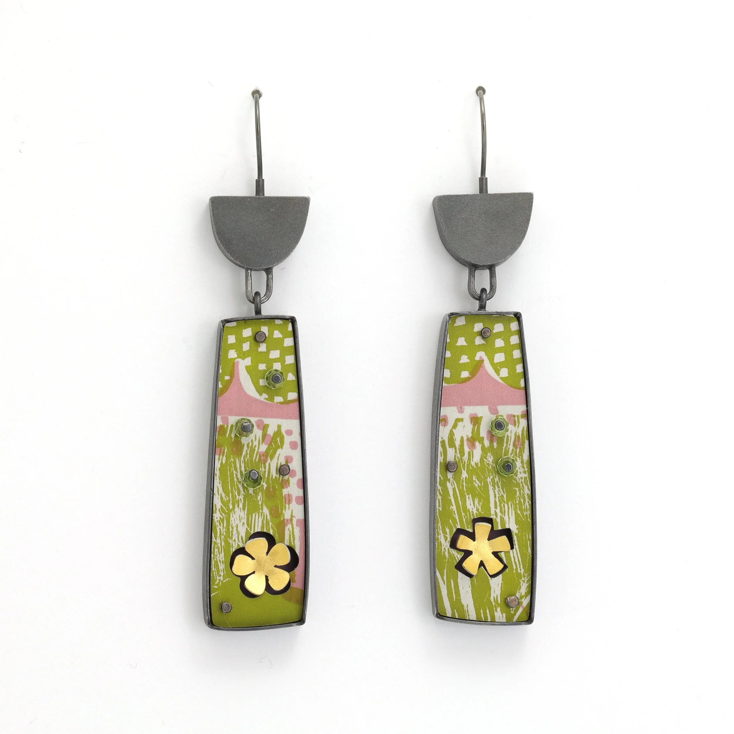 Pair of colorful earrings with a green and pink patterned design, flower-shaped cutouts at the bottom, attached to dark silver hooks.