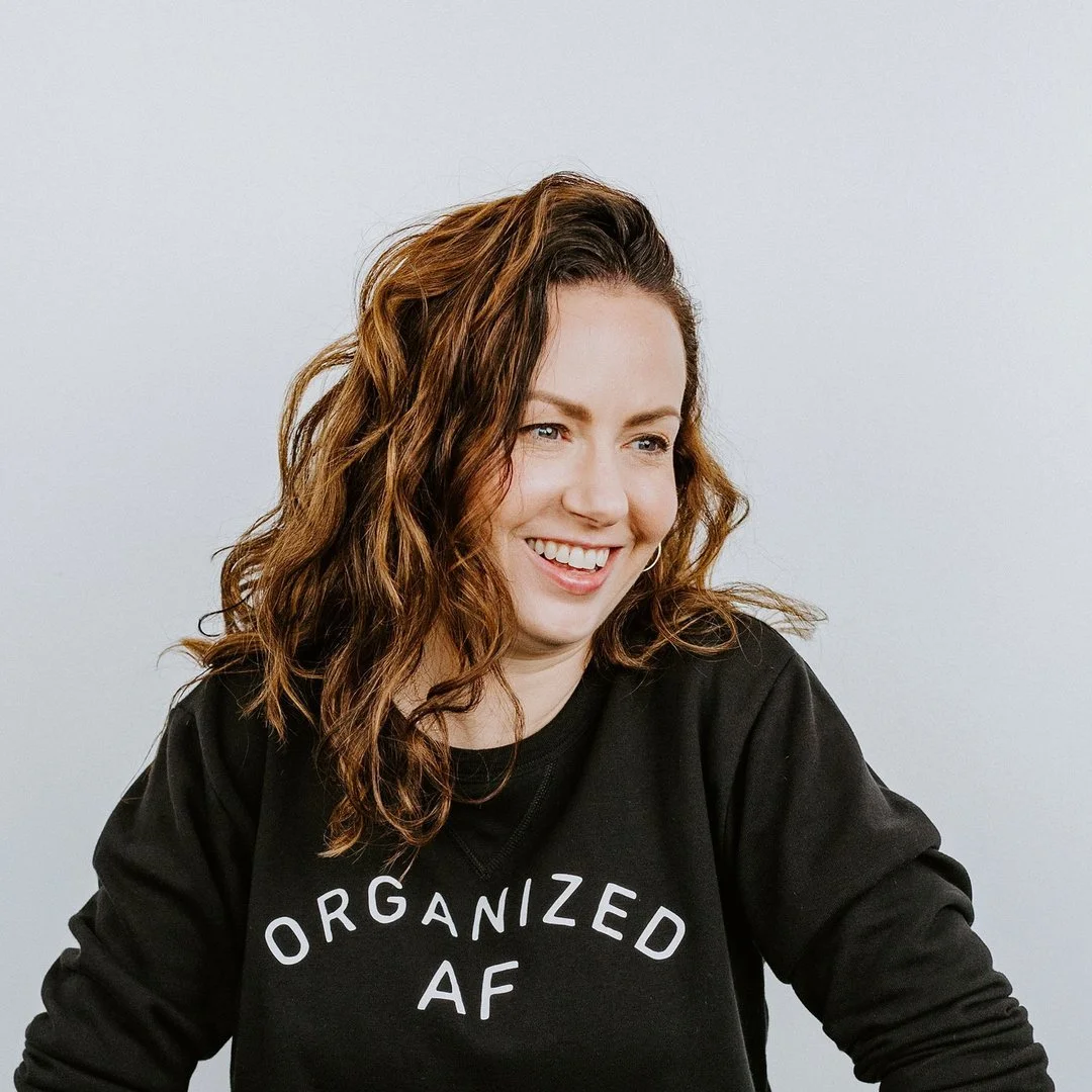 Kelle smiling, wearing a black sweatshirt that says "Organized AF" in white letters, against a plain light gray background.