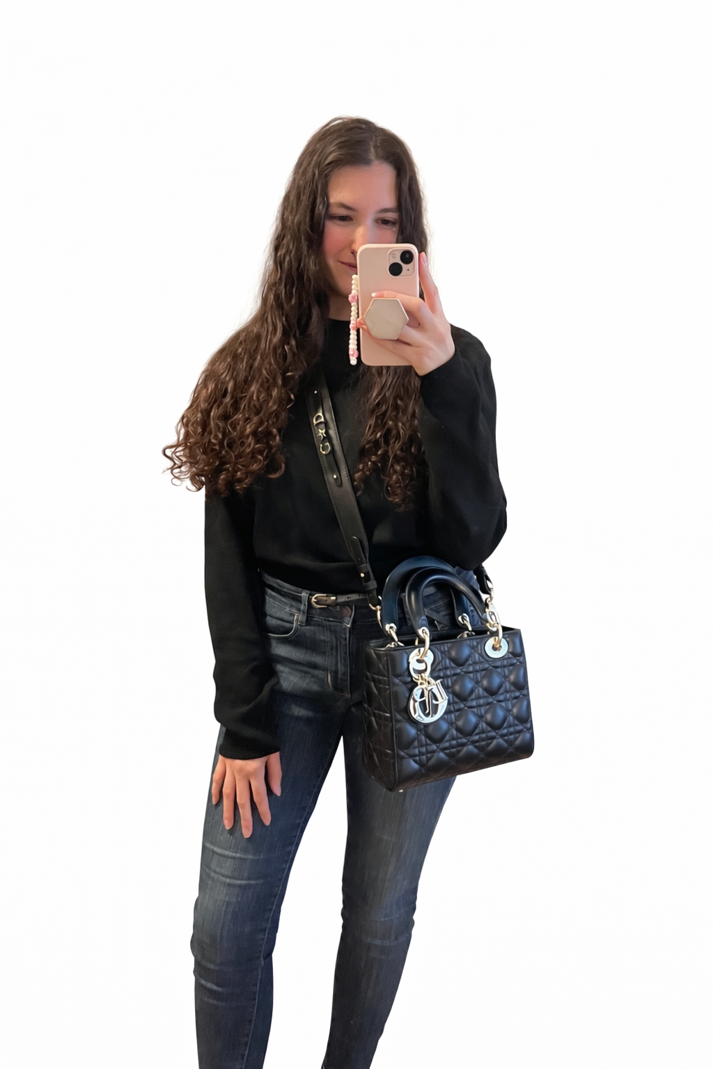 Young woman taking a mirror selfie with her smartphone, dressed in black top and jeans, carrying a black quilted handbag.