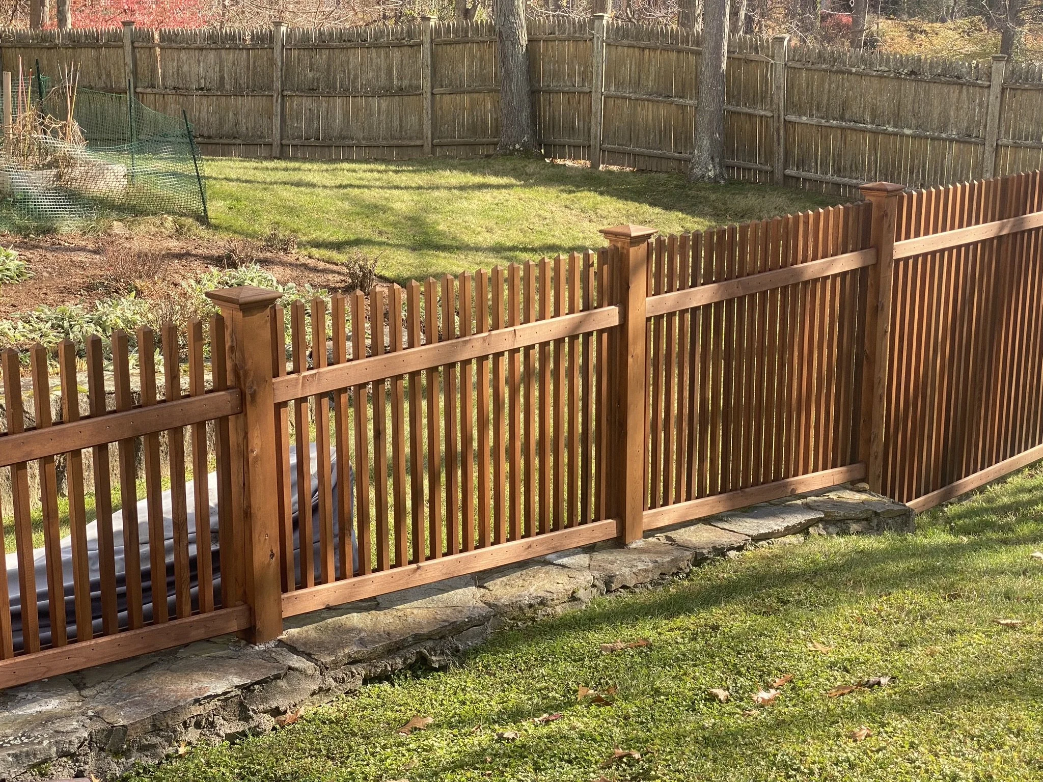 Wooden privacy fence with stone foundation, surrounding a yard with grass and trees