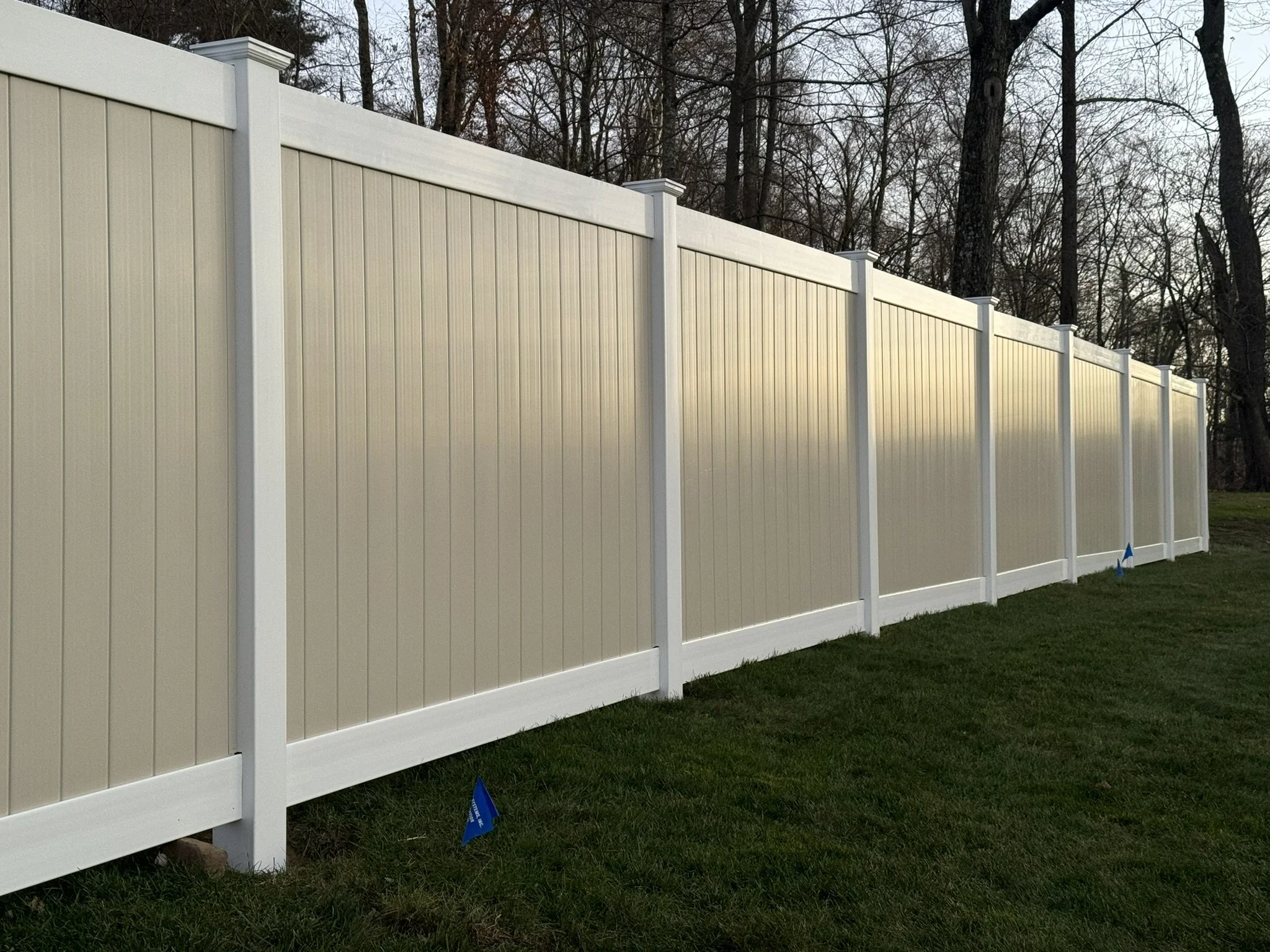 A white vinyl privacy fence installed on a grassy yard with trees in the background.