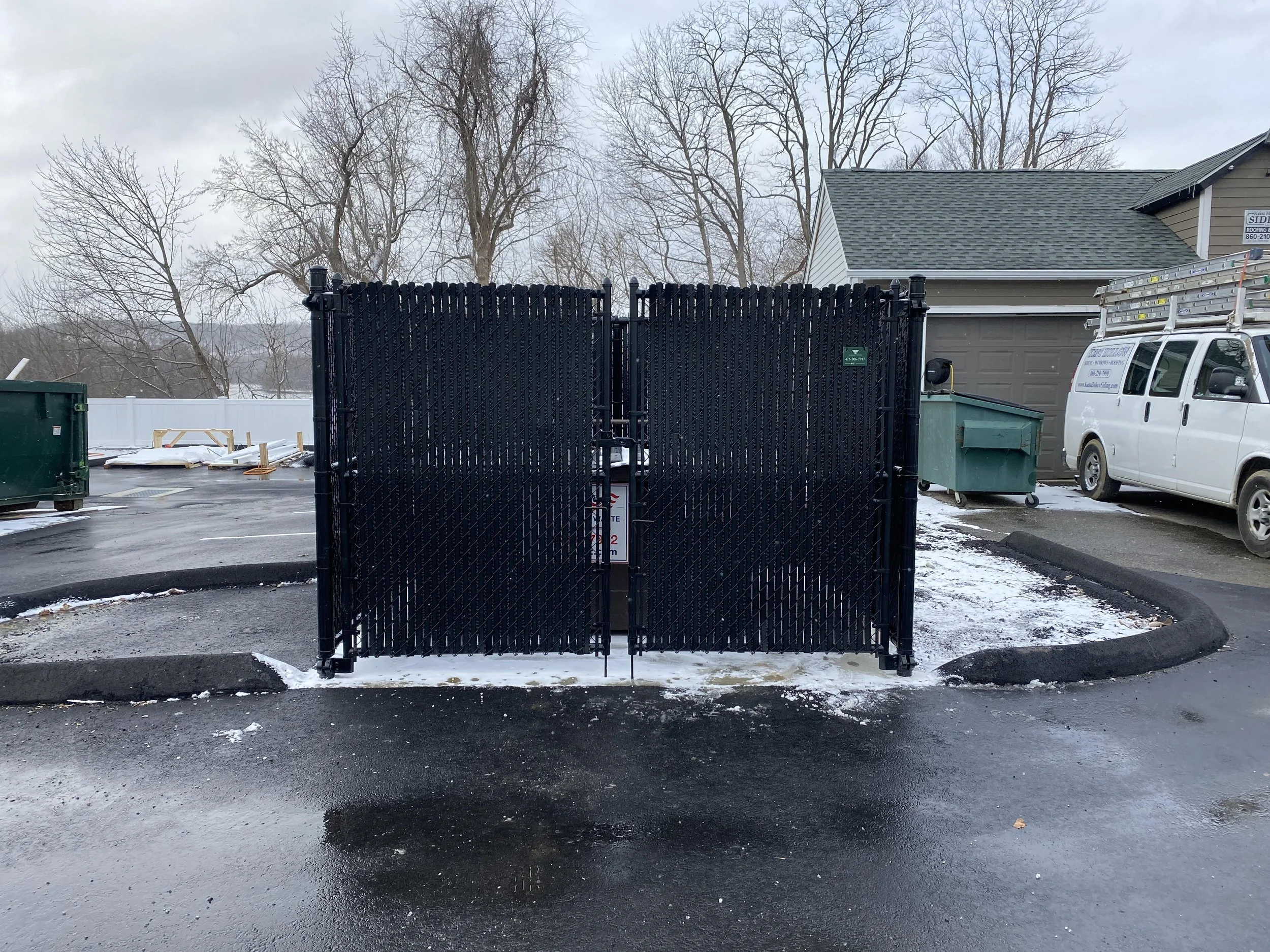 Black metal gate in a parking lot with snow, adjacent to a white utility van and a residential garage.