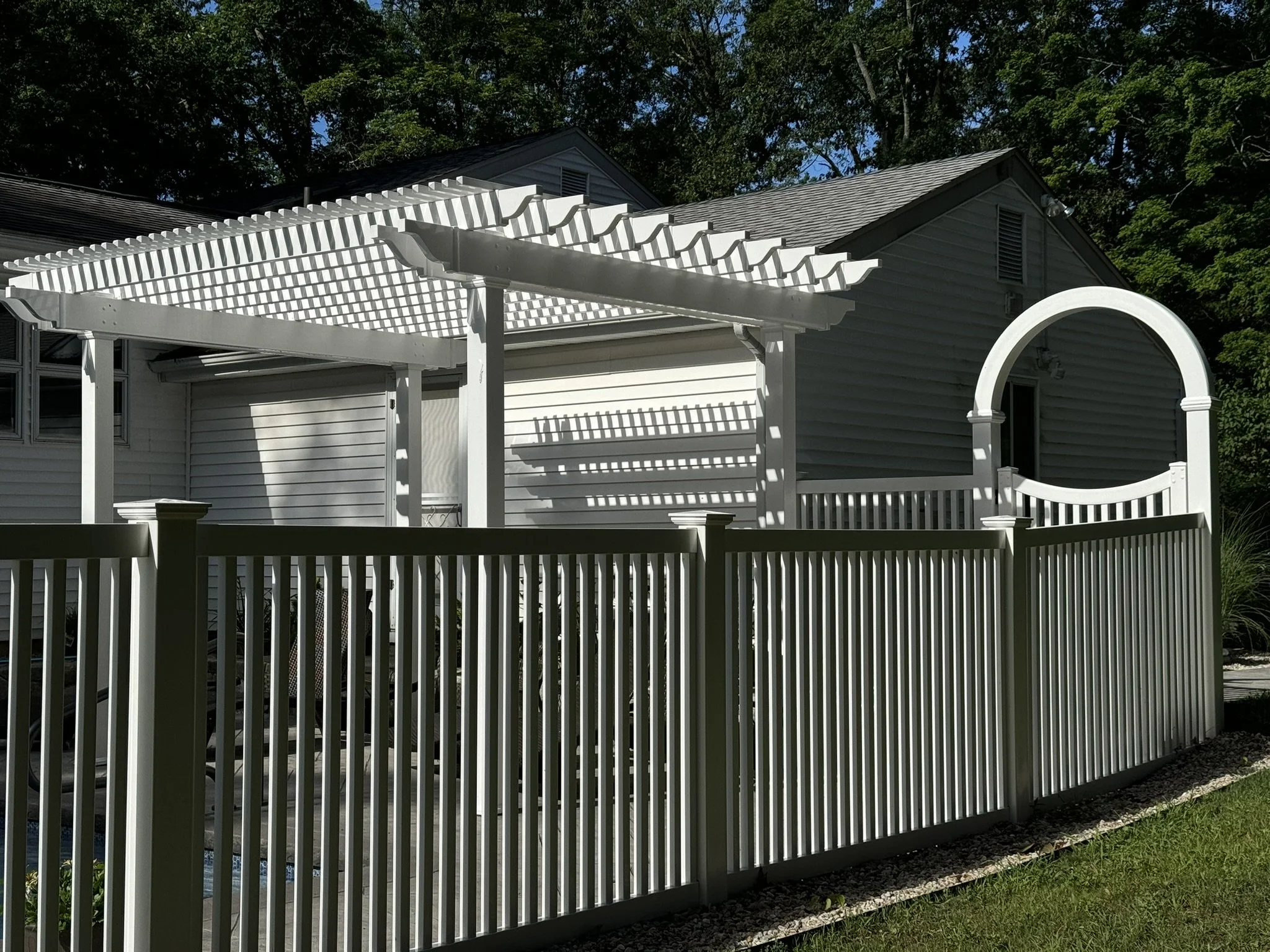 White backyard fence surrounding a house with a white pergola and arbor