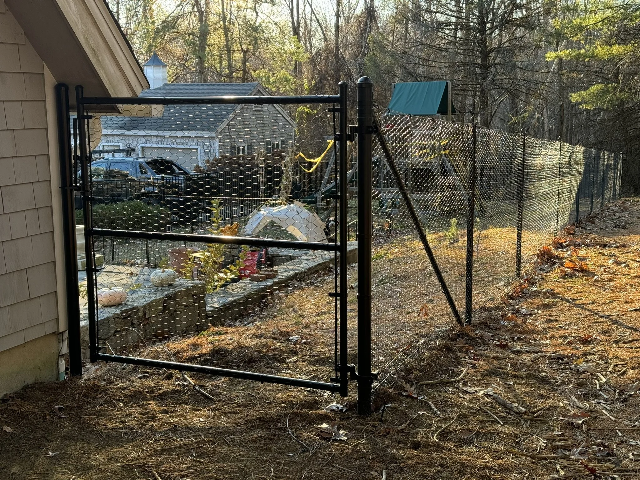 A black metal fence with honeycomb wire mesh is installed in a yard, with a swing set and wooded area in the background.