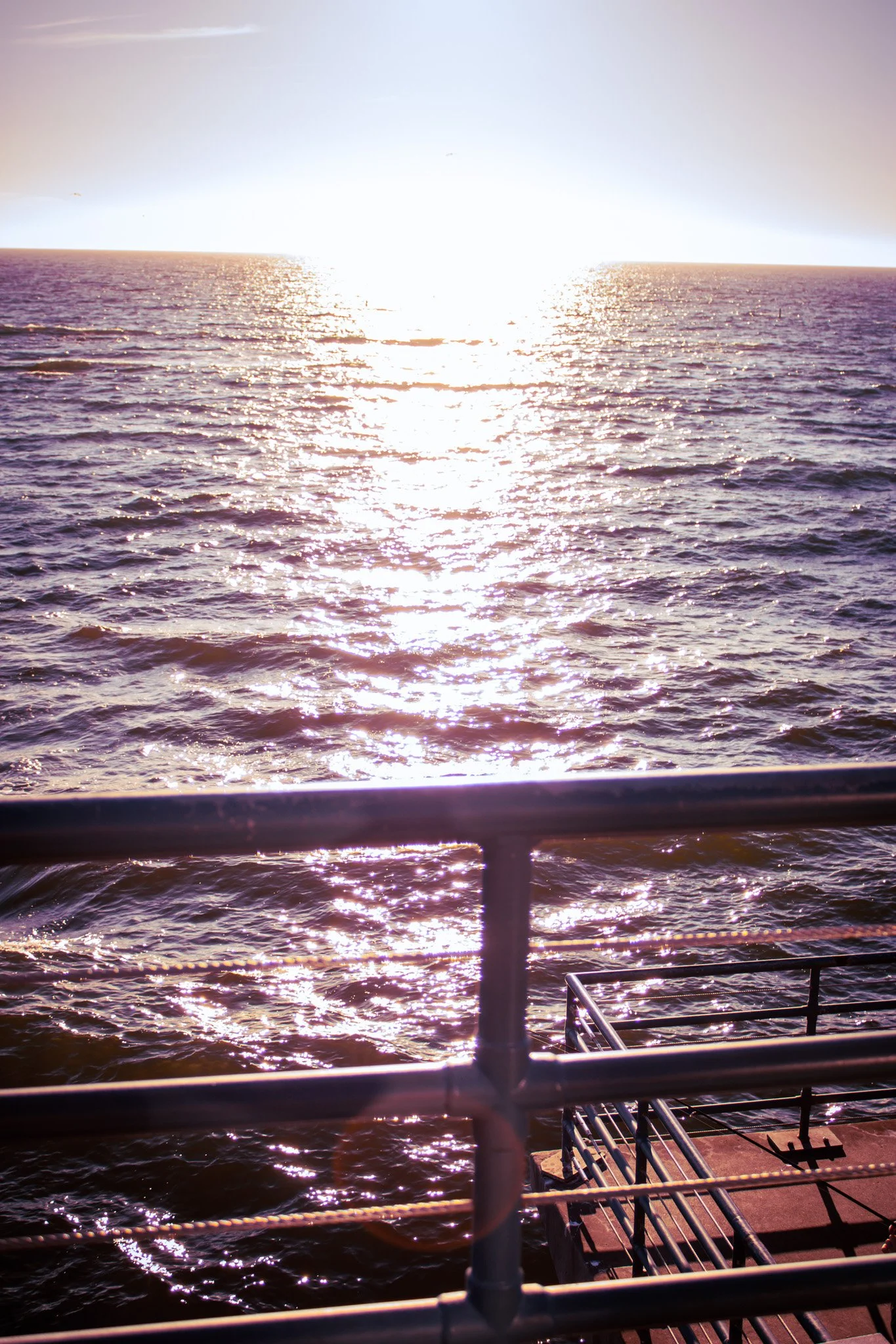 Sunset over the ocean as viewed from a boat, with railing and deck in the foreground.