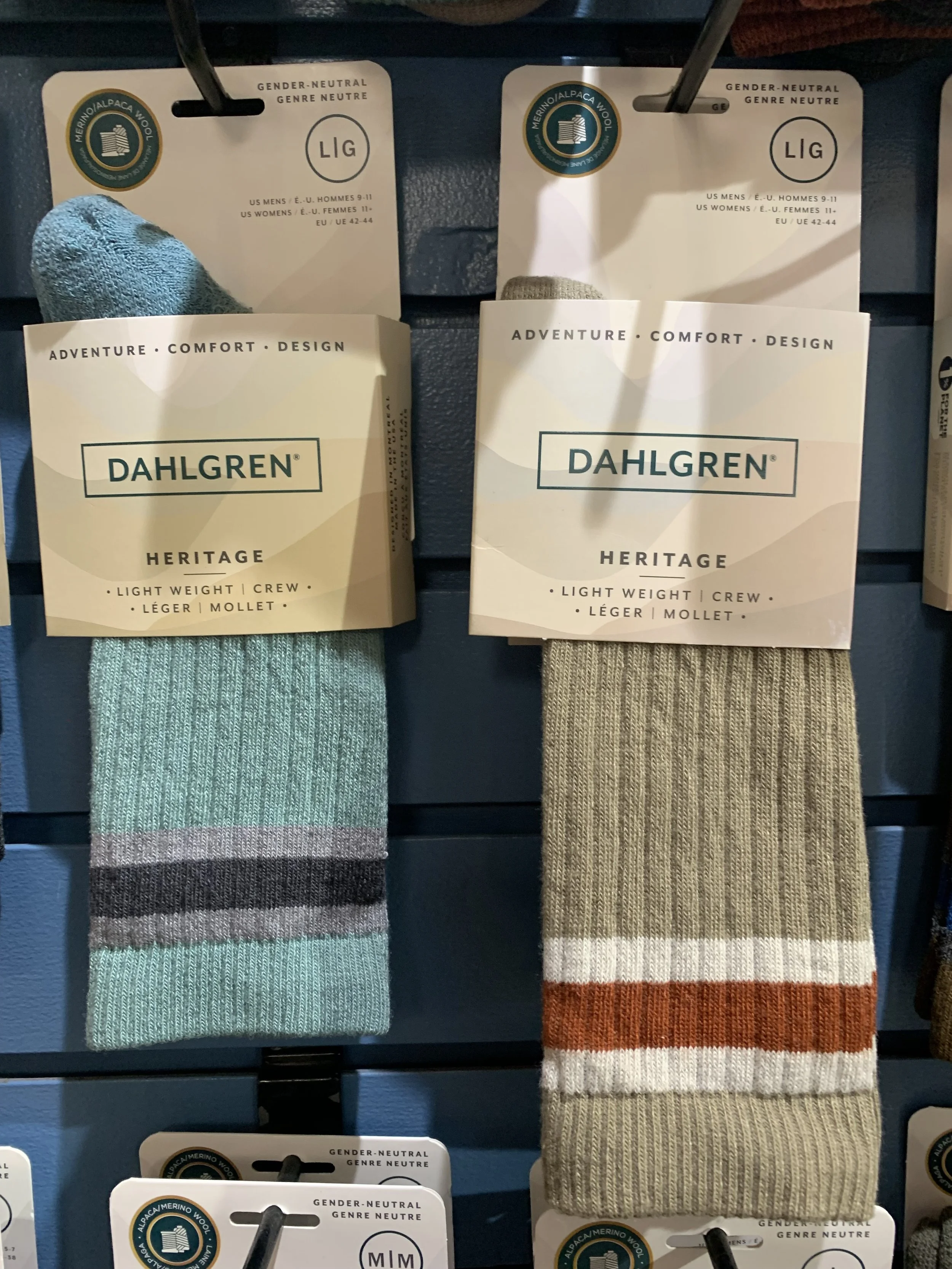 Two pairs of Dalhgren Heritage wool socks in retail display, one pair is teal with gray and black stripes, the other pair is beige with rust and white stripes.