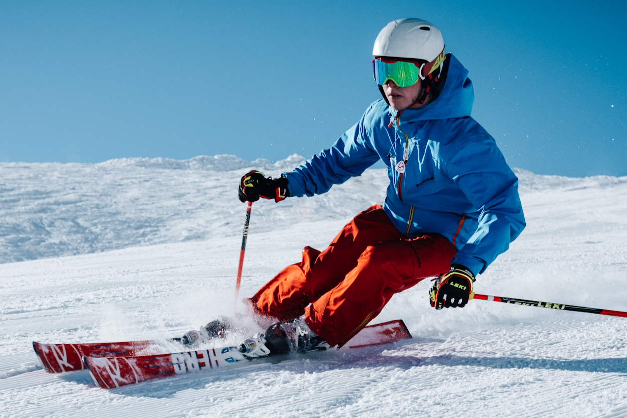 A skier in a blue jacket, red pants, a white helmet, and reflective goggles skiing down a snow-covered slope.