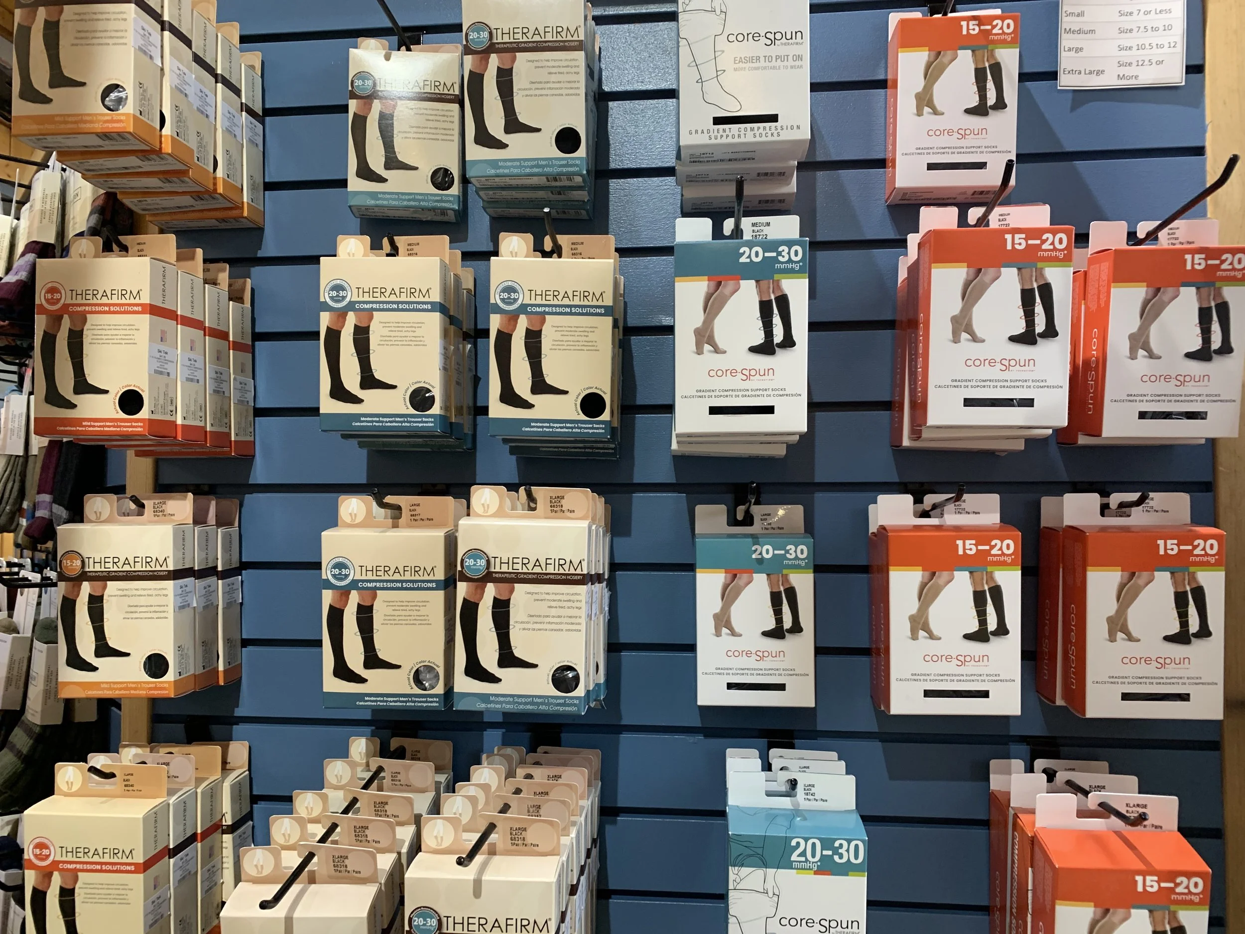 Display of compression support socks in a store with various brands and sizes, arranged on a slatwall with hooks.