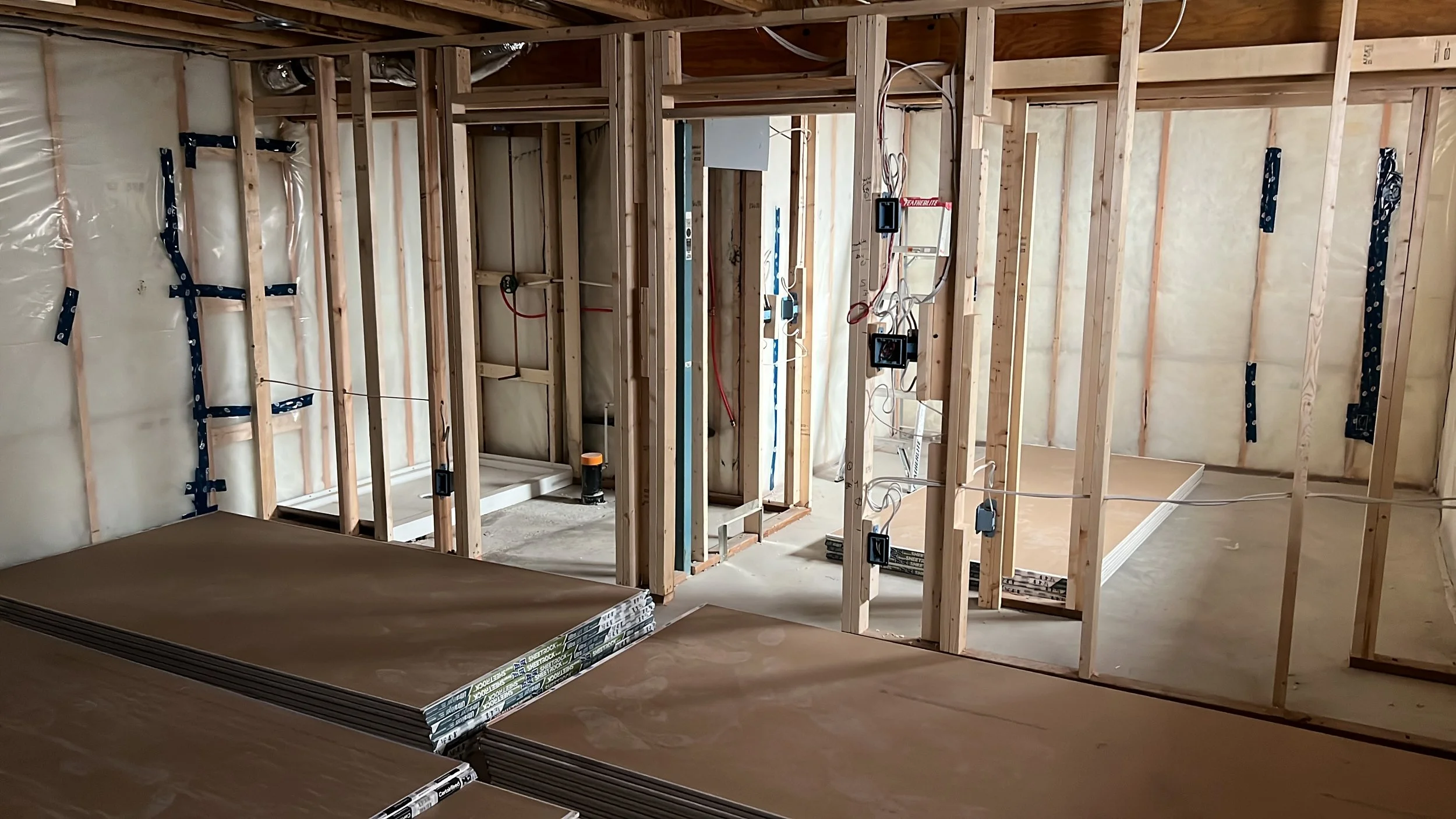 Interior view of a house under construction showing unfinished wooden framed walls, electrical wiring, and construction materials on the floor.