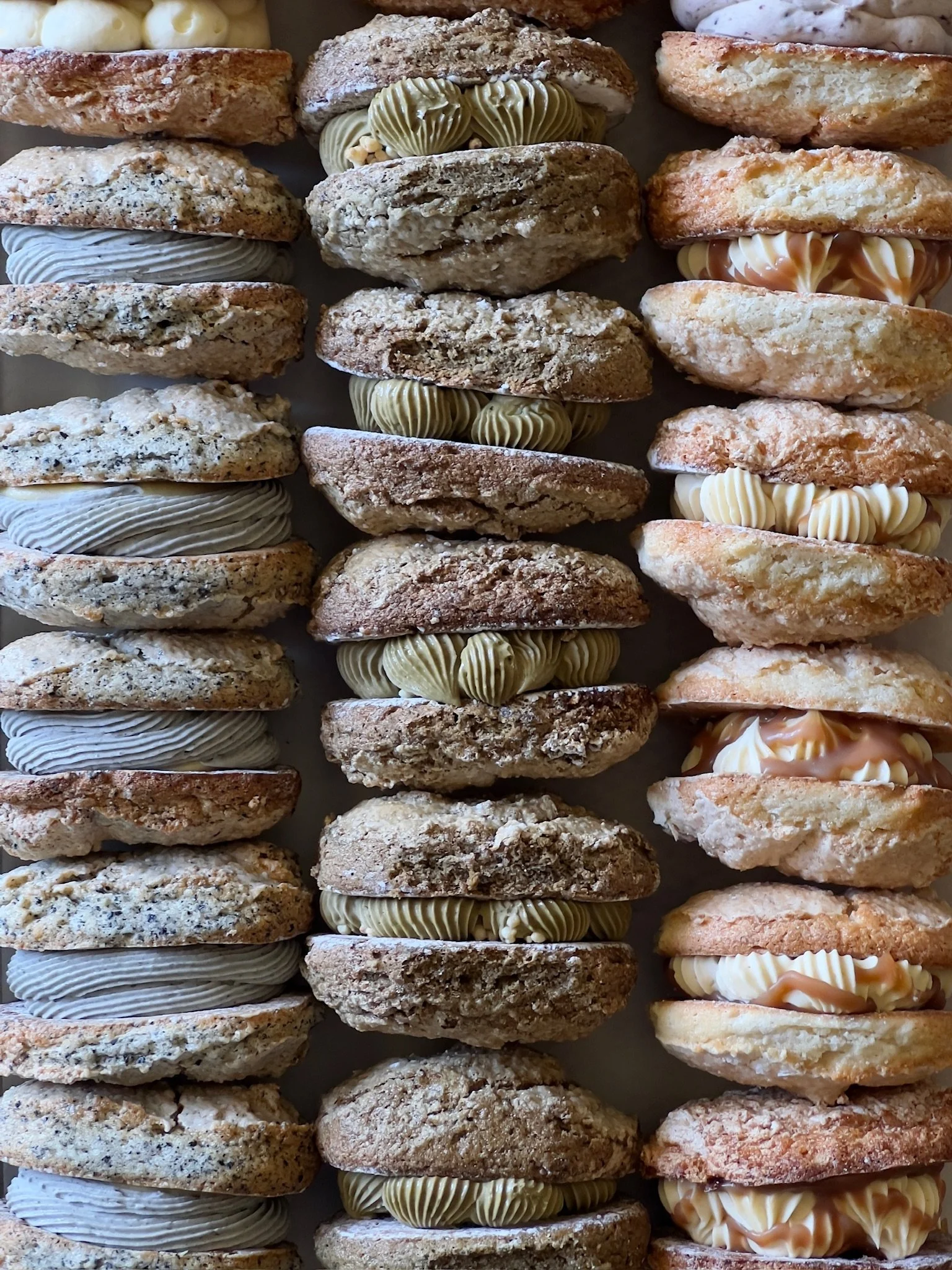 Row of assorted sandwich cookies with various fillings and toppings.