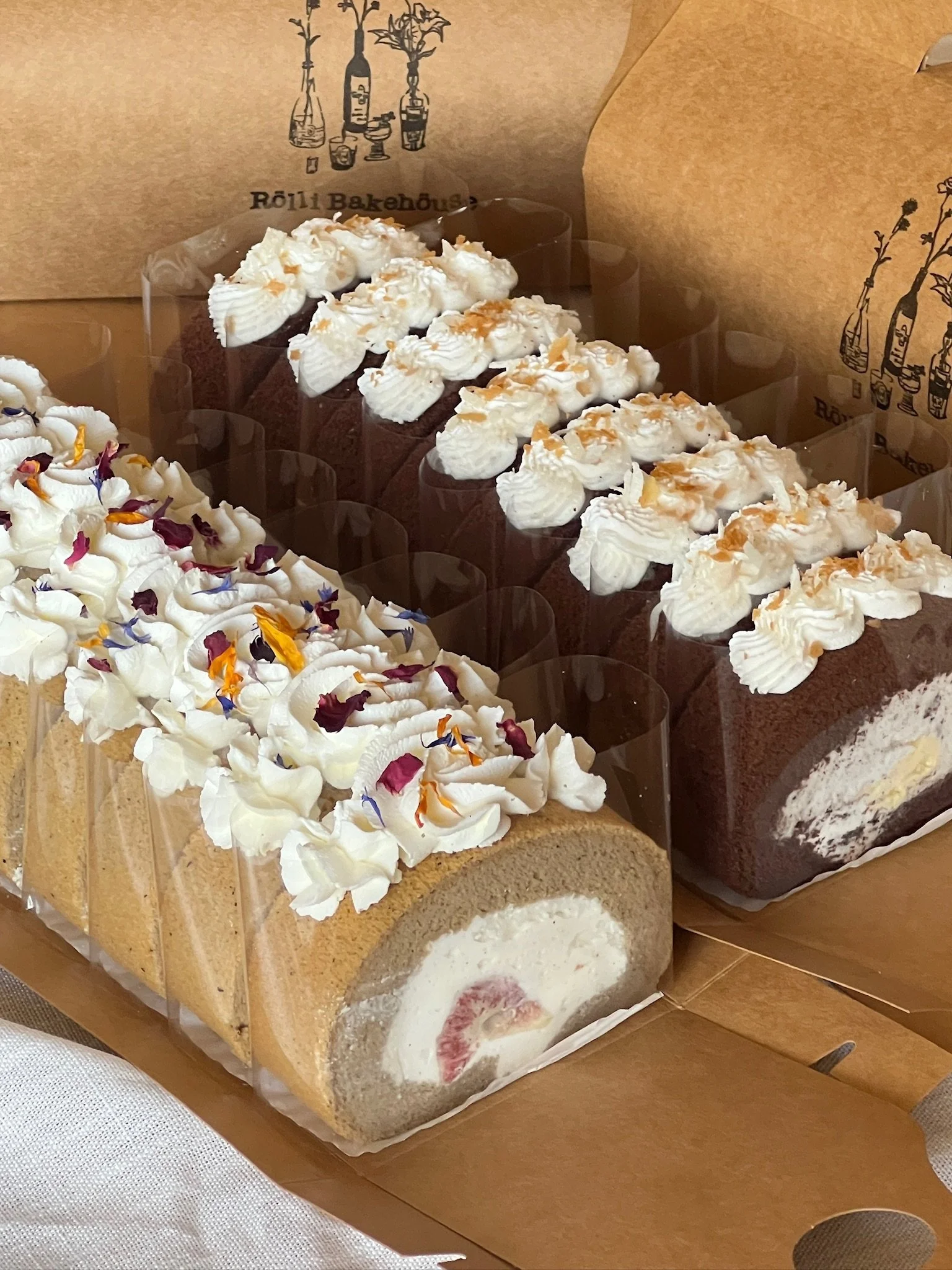 Two rolls with whipped cream and edible flowers, and two slices of chocolate cake with whipped cream and caramel drizzle.