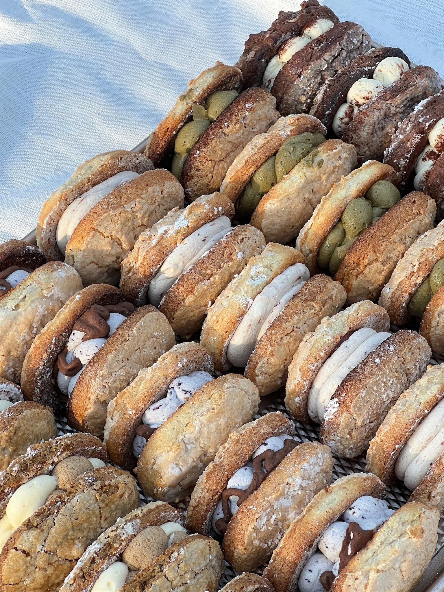 A tray of assorted cookies filled with various fillings including chocolate, cream, and what appears to be jam, decorated with nuts and candies.
