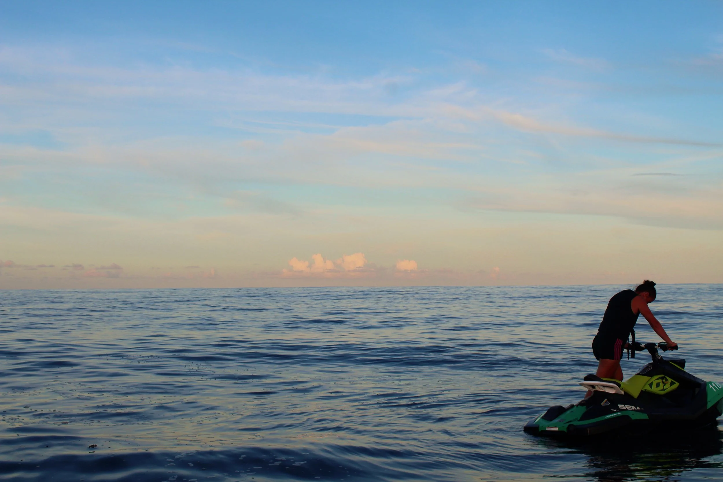 Person preparing a jet ski on calm ocean water during sunset or sunrise.
