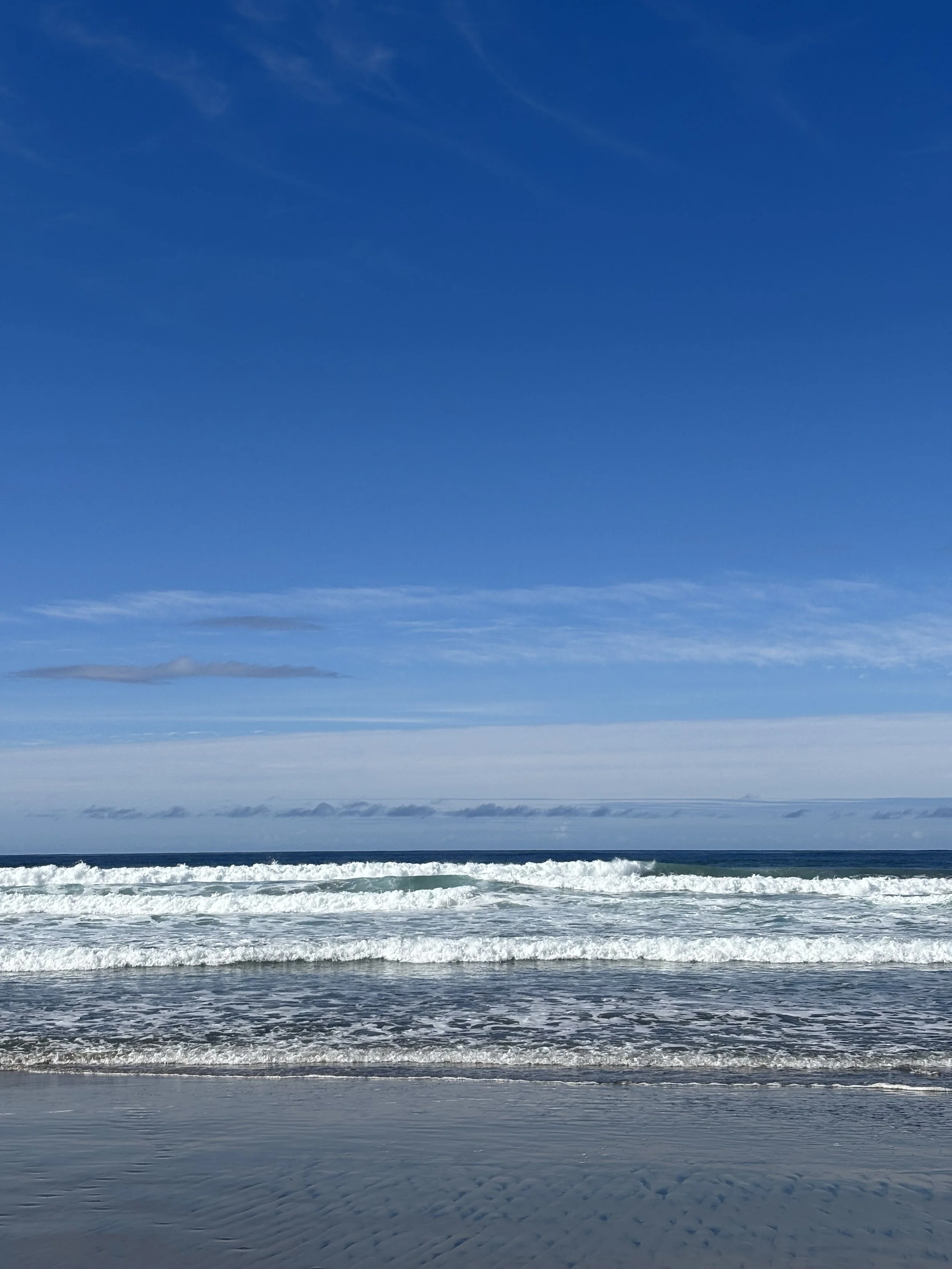Ocean waves crashing onto the sandy beach with a clear blue sky overhead.