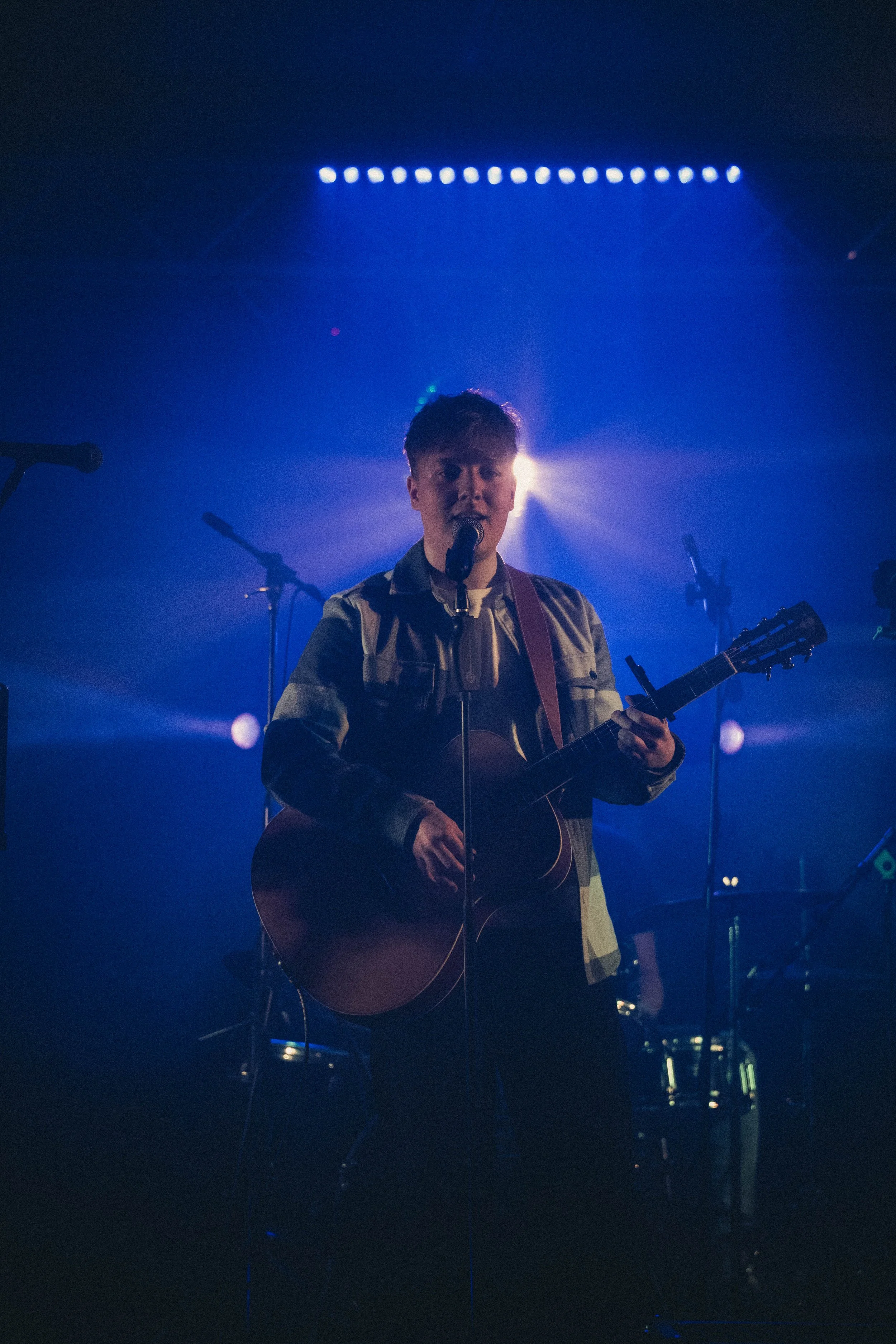 Musiker spielt Gitarre und singt auf einer Bühne mit blauen Lichtern im Hintergrund.