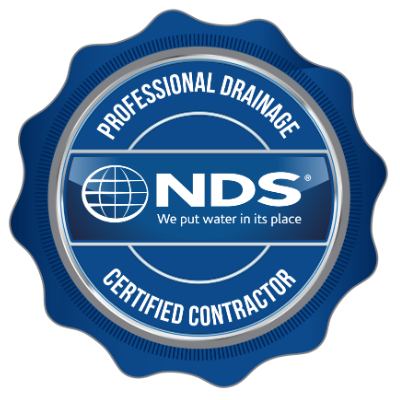A circular badge with a dark blue border and light blue inner circle. The badge features the NDS logo with a globe icon and the text "We put water in its place". The outer ring says "Professional Drainage Certified Contractor."