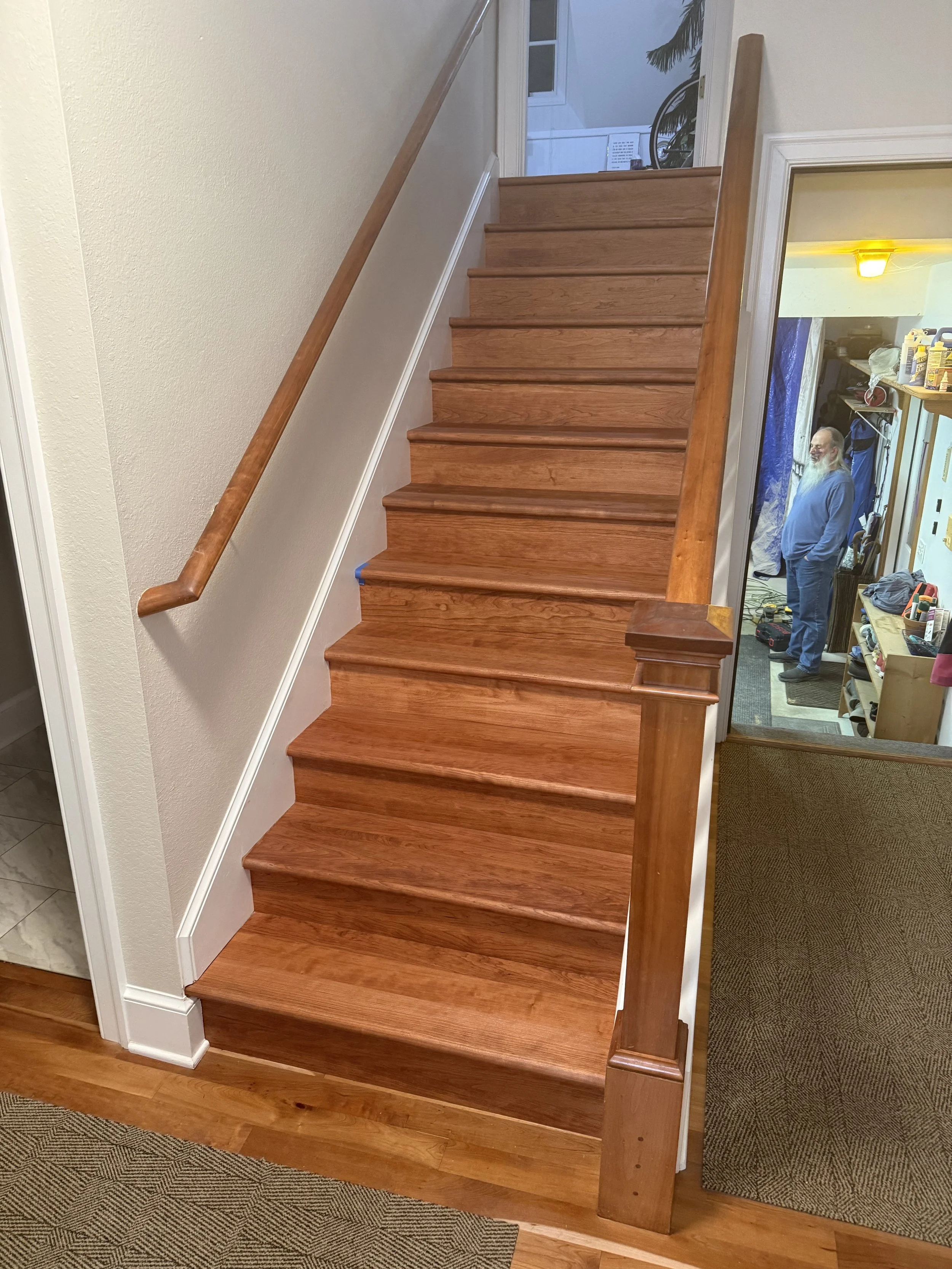 A staircase with wooden steps and matching wooden handrail next to an off-white wall.