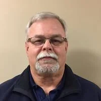 A scenic sunrise over a lush, green field with trees and wildflowers, mist in the background, and sunlight filtering through the trees.