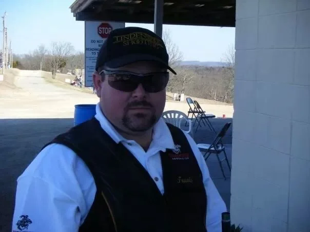A rural road runs through green fields on both sides, with a large, partly cloudy sky overhead during daytime.