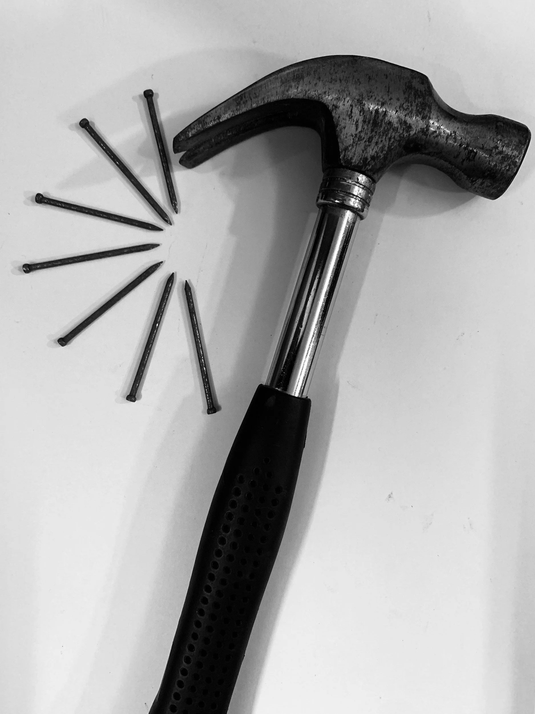 A hammer with a black handle and metal head, alongside eight nails on a white surface.