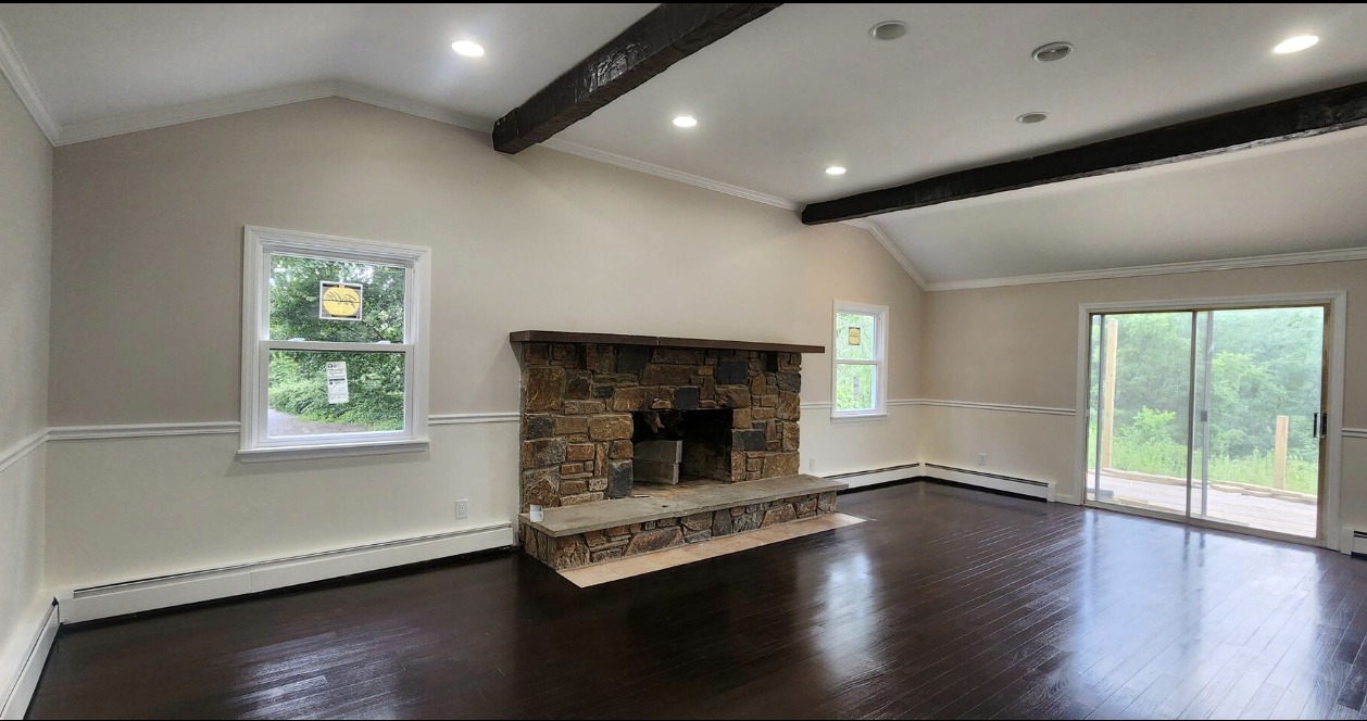 Empty living room with a stone fireplace, dark wooden floor, white walls, and large sliding glass door leading to an outdoor deck.