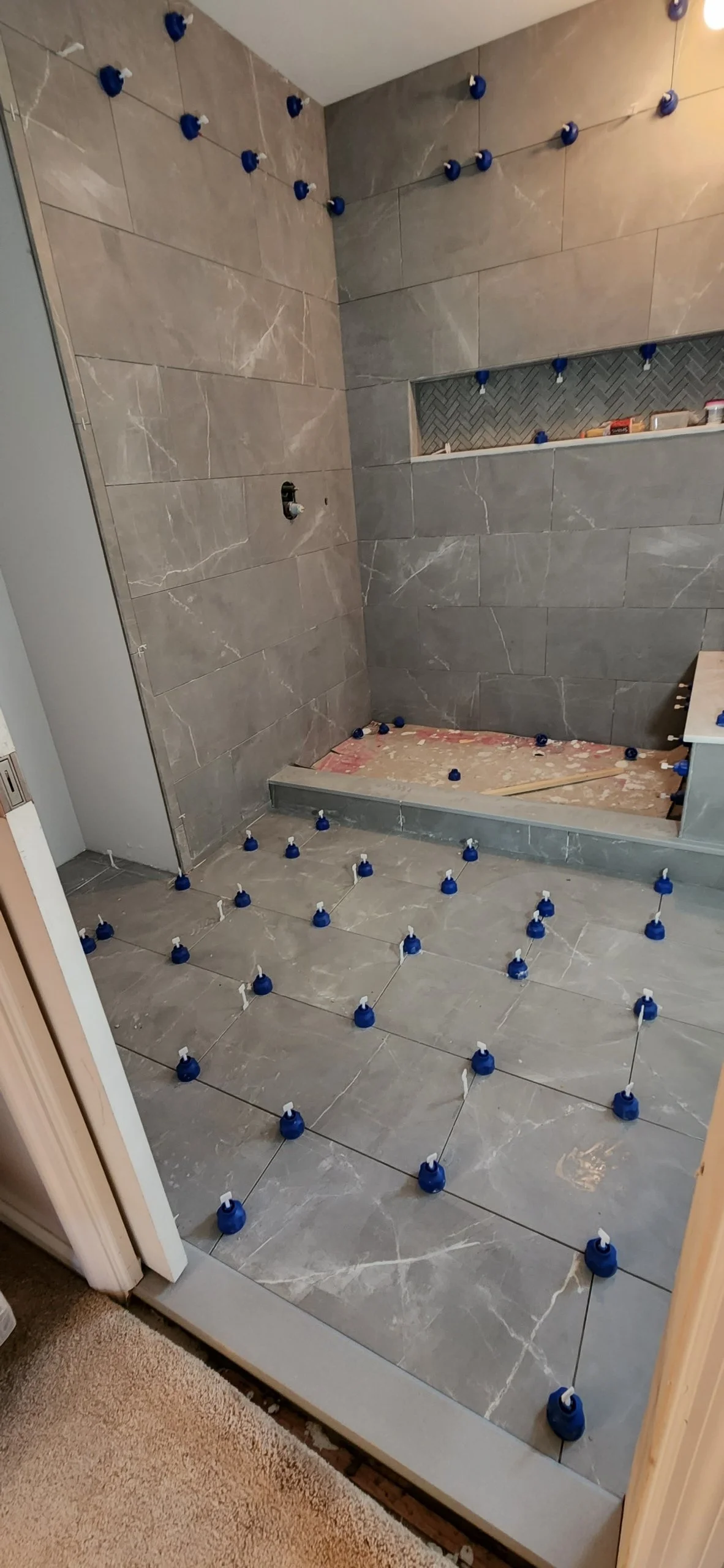 Newly tiled bathroom shower area with blue and white tile spacers still in place, indicating ongoing construction or renovation work.