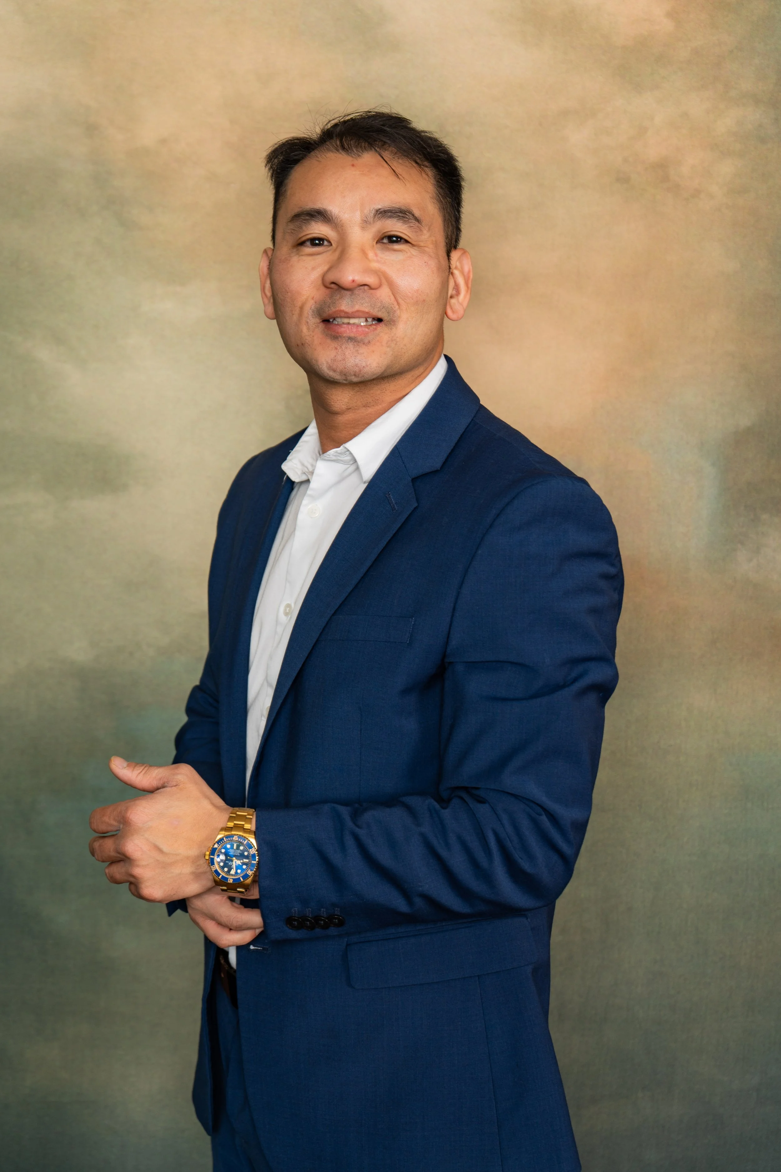 A man in a navy blue suit and white shirt standing against a multicolored background.