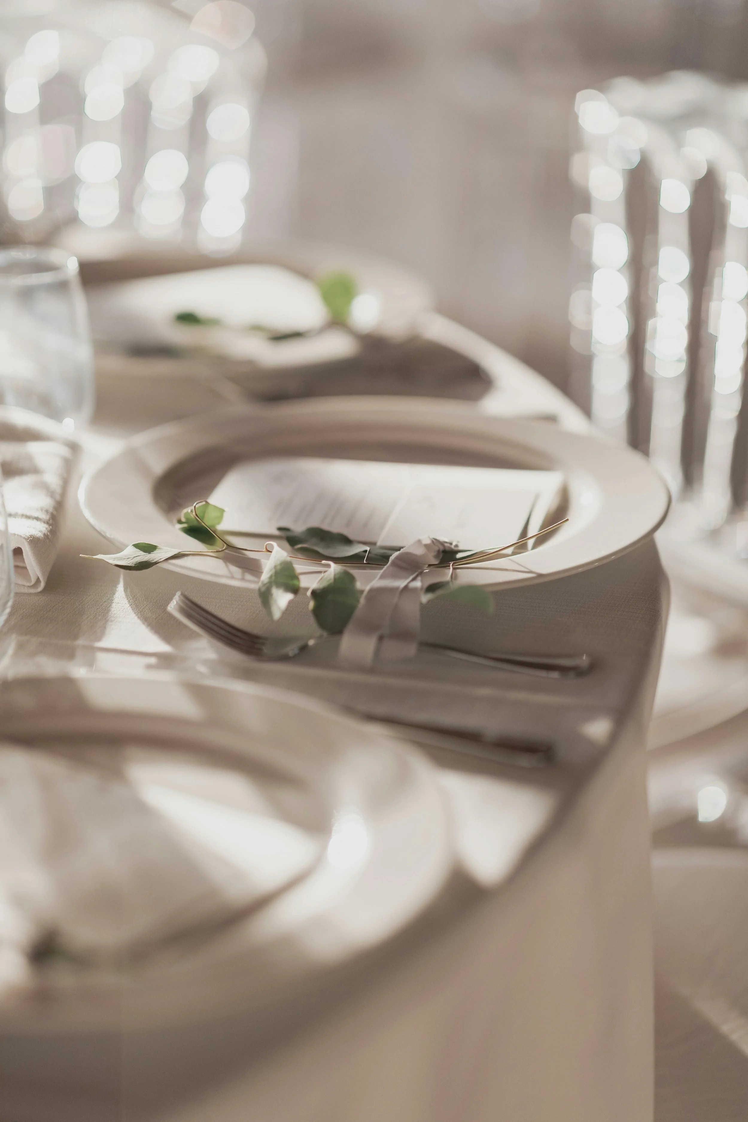 Elegant table setting with white plates, silverware, a menu, and greenery decor.