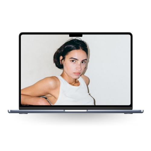 A young woman with short dark hair and a white sleeveless top looking at the camera, shown on a laptop screen.