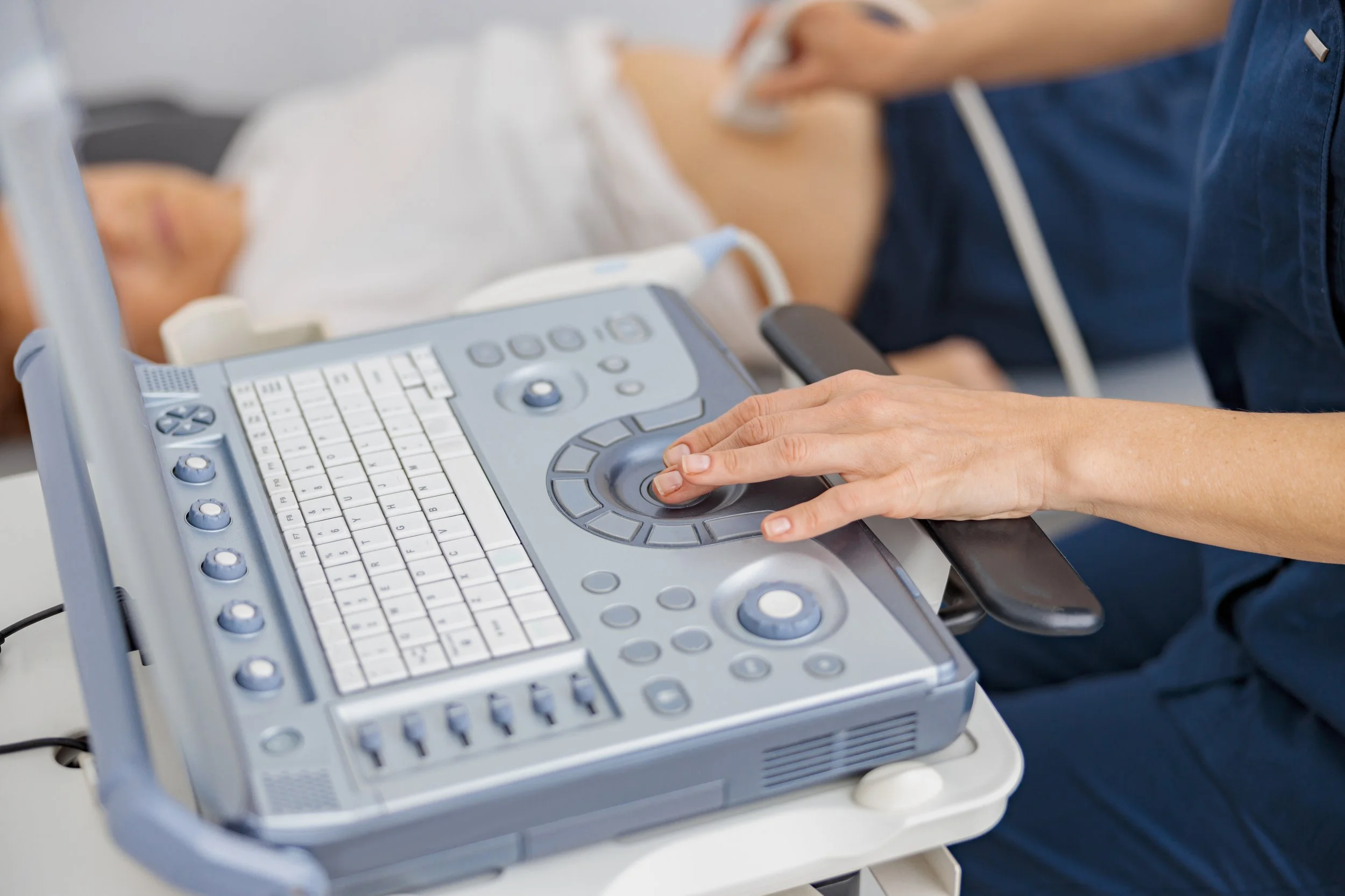 Hospital staff performing an ultrasound on a patient lying in bed, with ultrasound machine and patient in the background.