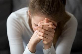 A woman with brown hair praying or distressed, with her hands clasped and head bowed.