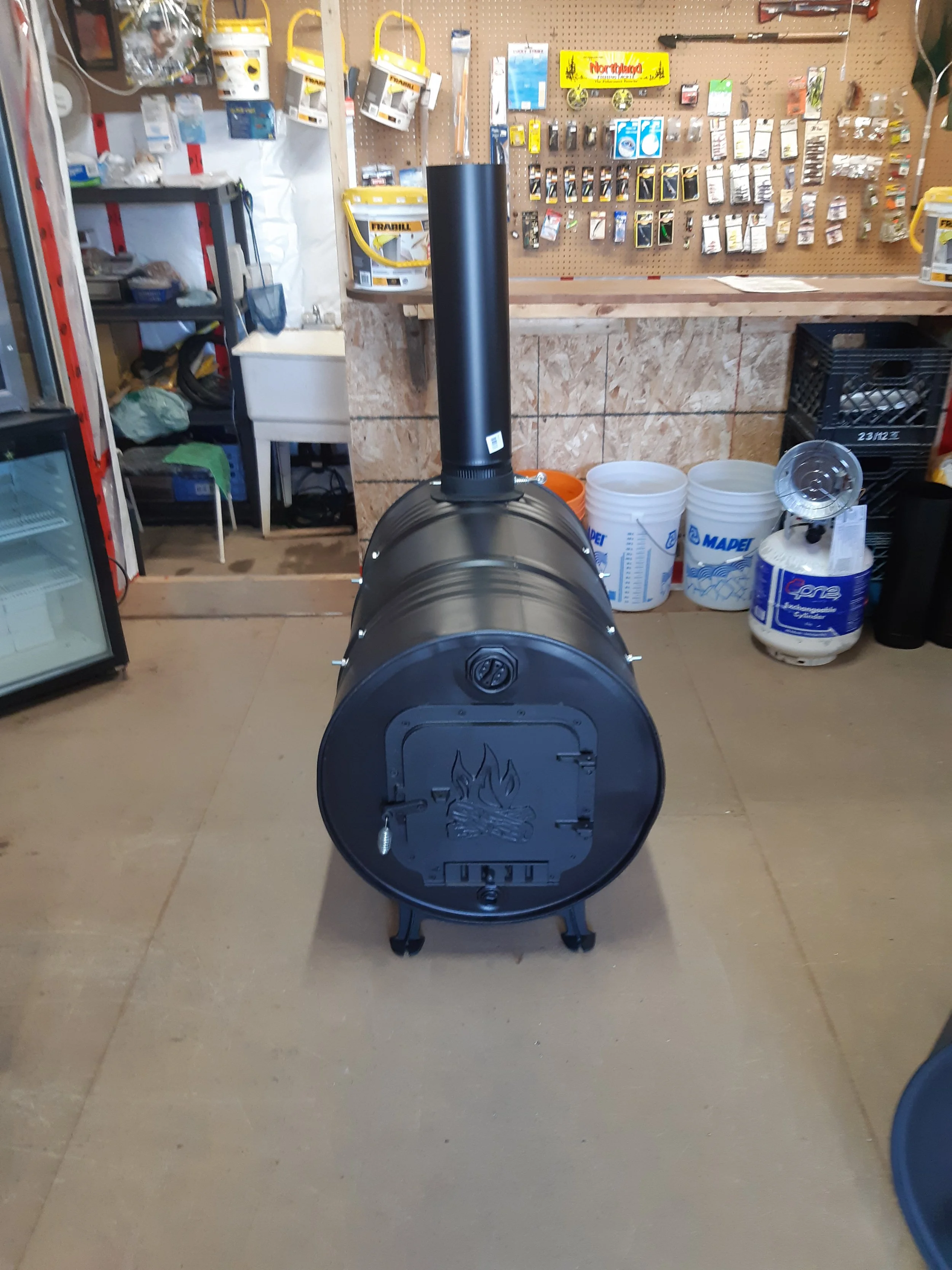Black outdoor wood-burning stove with a chimney, metal door with a fire logo, in a hardware store.