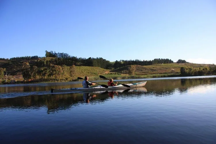 Two people kayaking on the lake at Oneiric, with green hillside and clear blue sky in background.